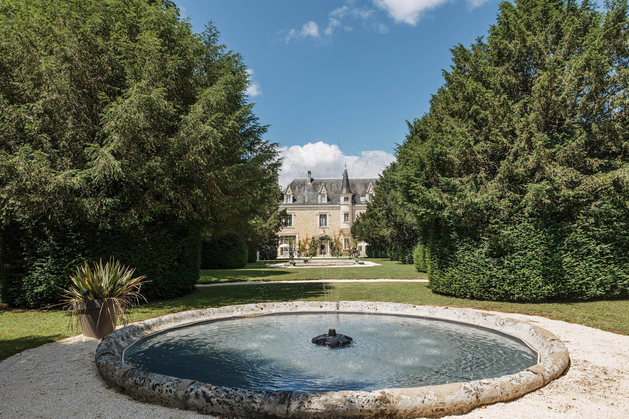 French chateau with slate mansard roof and turret viewed from formal garden with stone fountain and clipped hedges