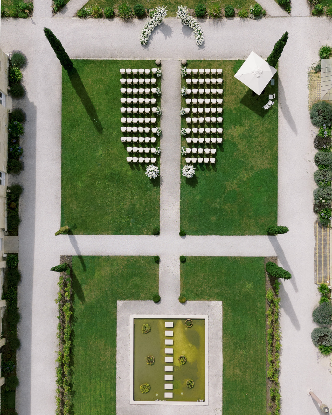 Aerial view of formal garden ceremony setup with white Chiavari chairs arranged symmetrically on lawn with boxwood borders