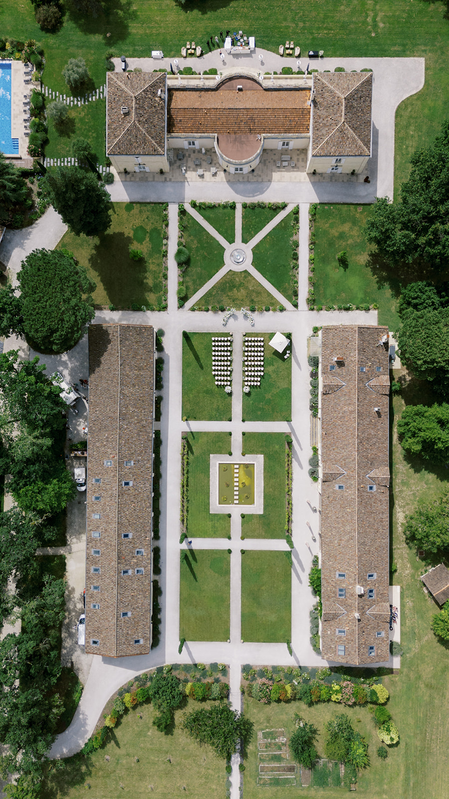 Aerial view of a classical chateau estate with formal gardens and ceremony seating arranged in the courtyard