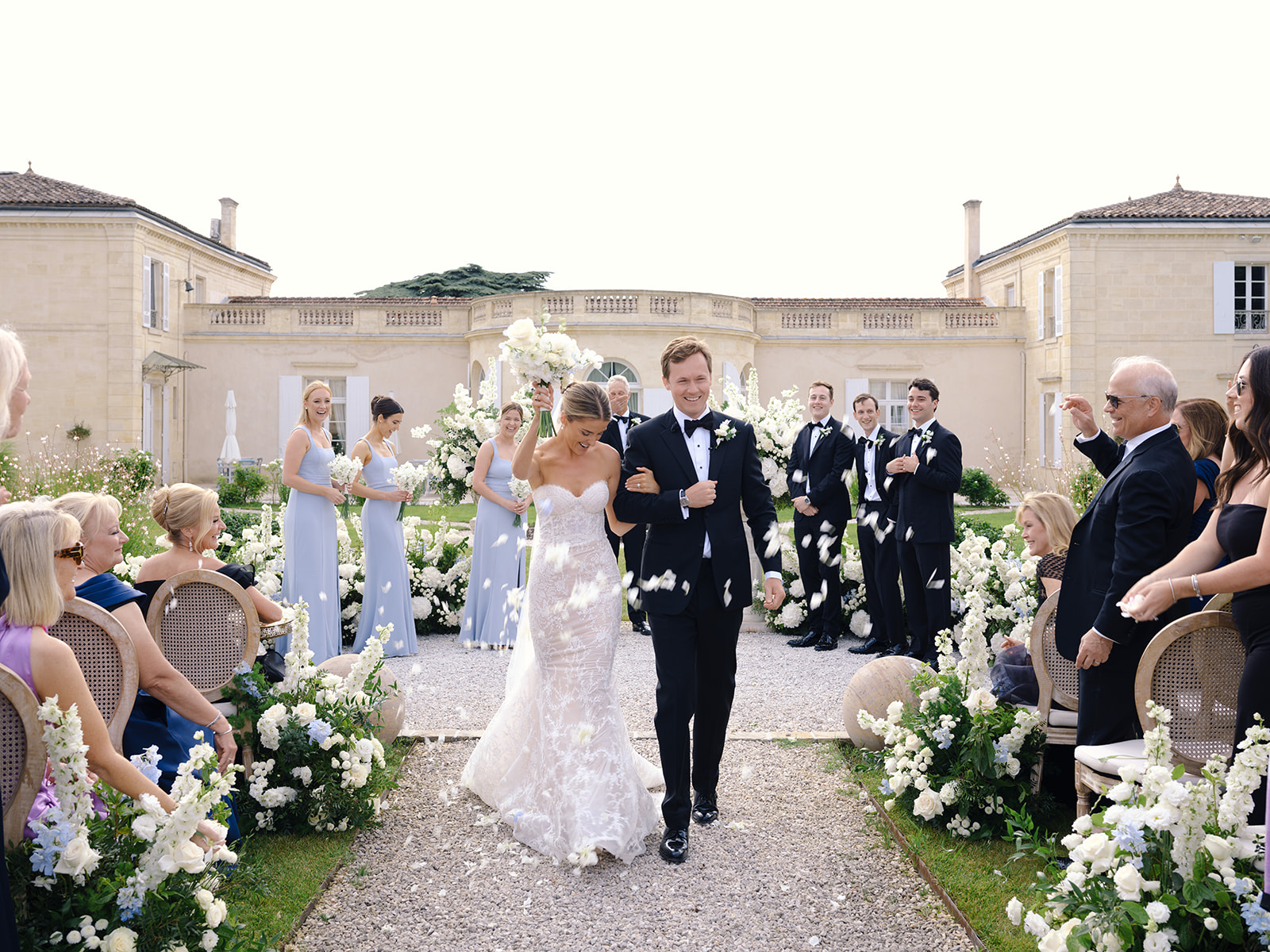 Bride and groom recessional at neoclassical chateau, bridesmaids in pale blue, groomsmen in black tuxedos
