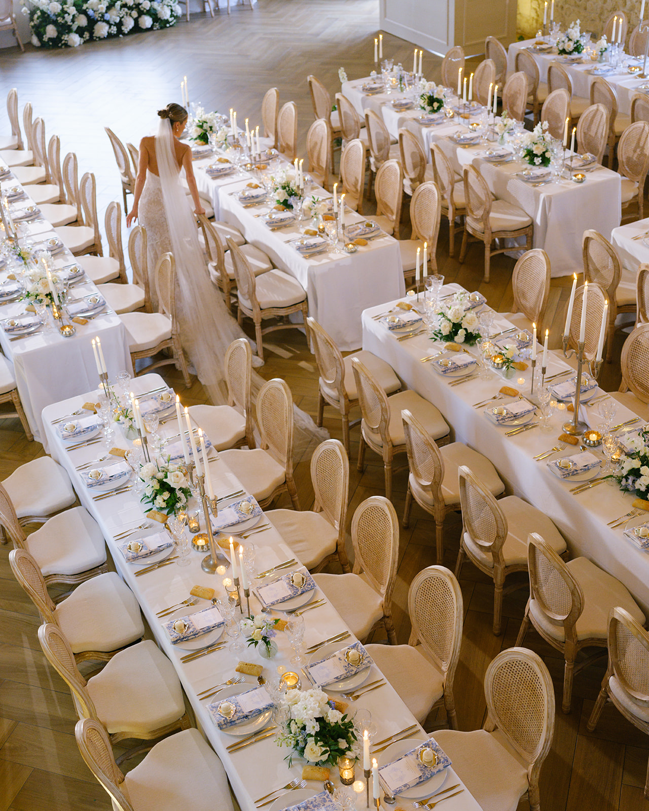 Reception tables set with ivory linens, gold flatware, cream candles, and low white and green floral centerpieces