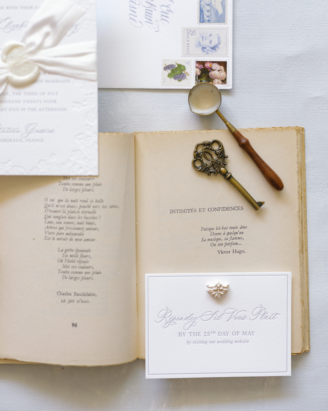 Flat lay of vintage French poetry book, RSVP card, wax seal, and antique brass key on gray surface