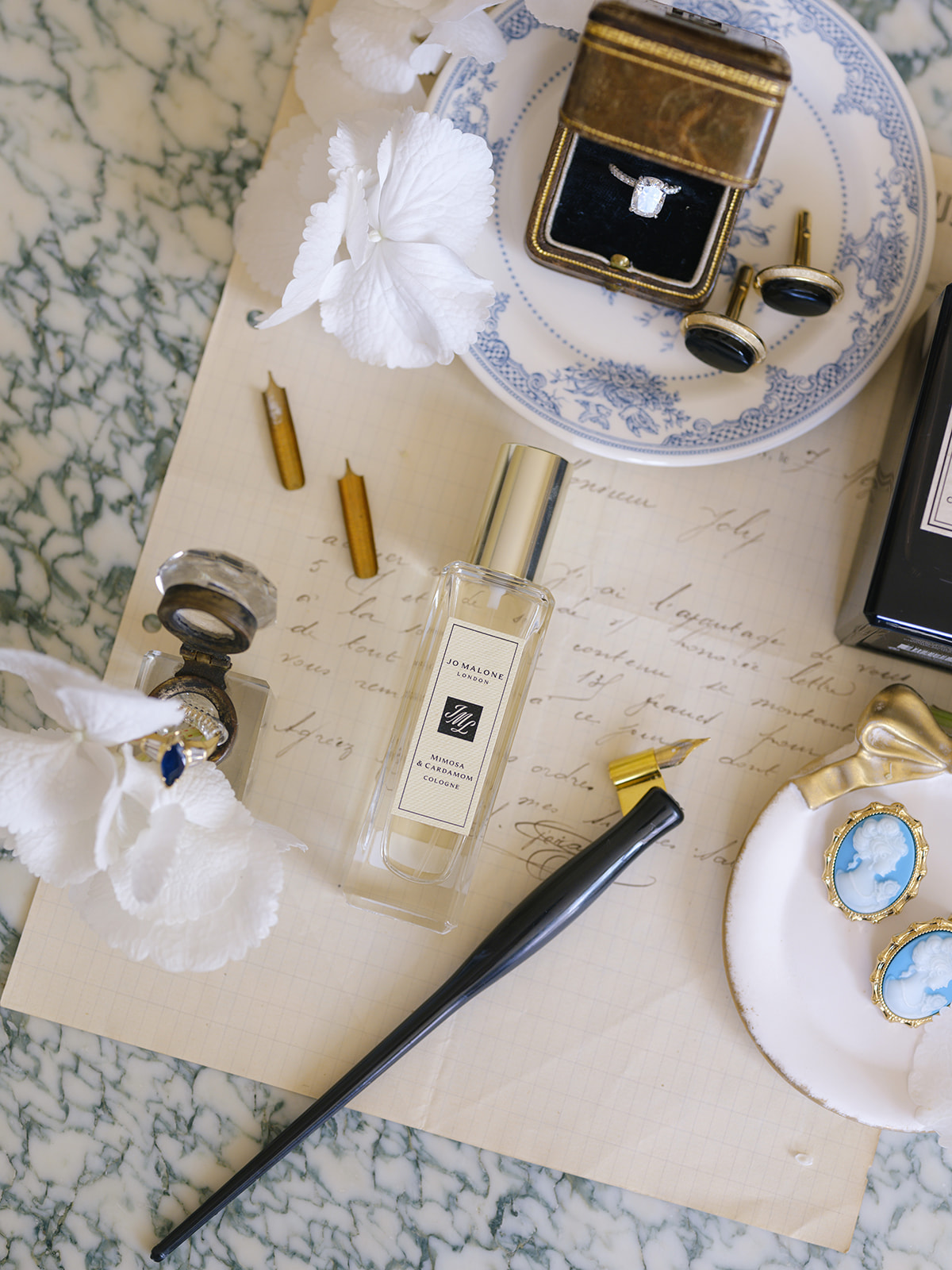 Bridal flat lay with toile plate, diamond ring in box, gold cufflinks, Jo Malone cologne, and vintage perfume
