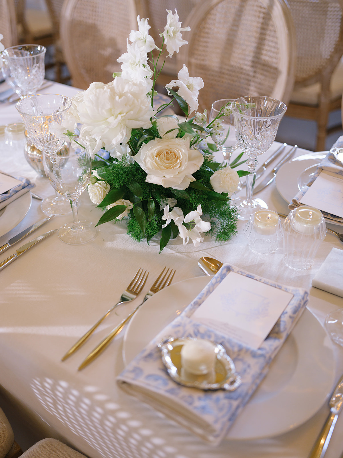 Reception centerpiece of ivory and champagne roses with white delphiniums and cream candles on round table