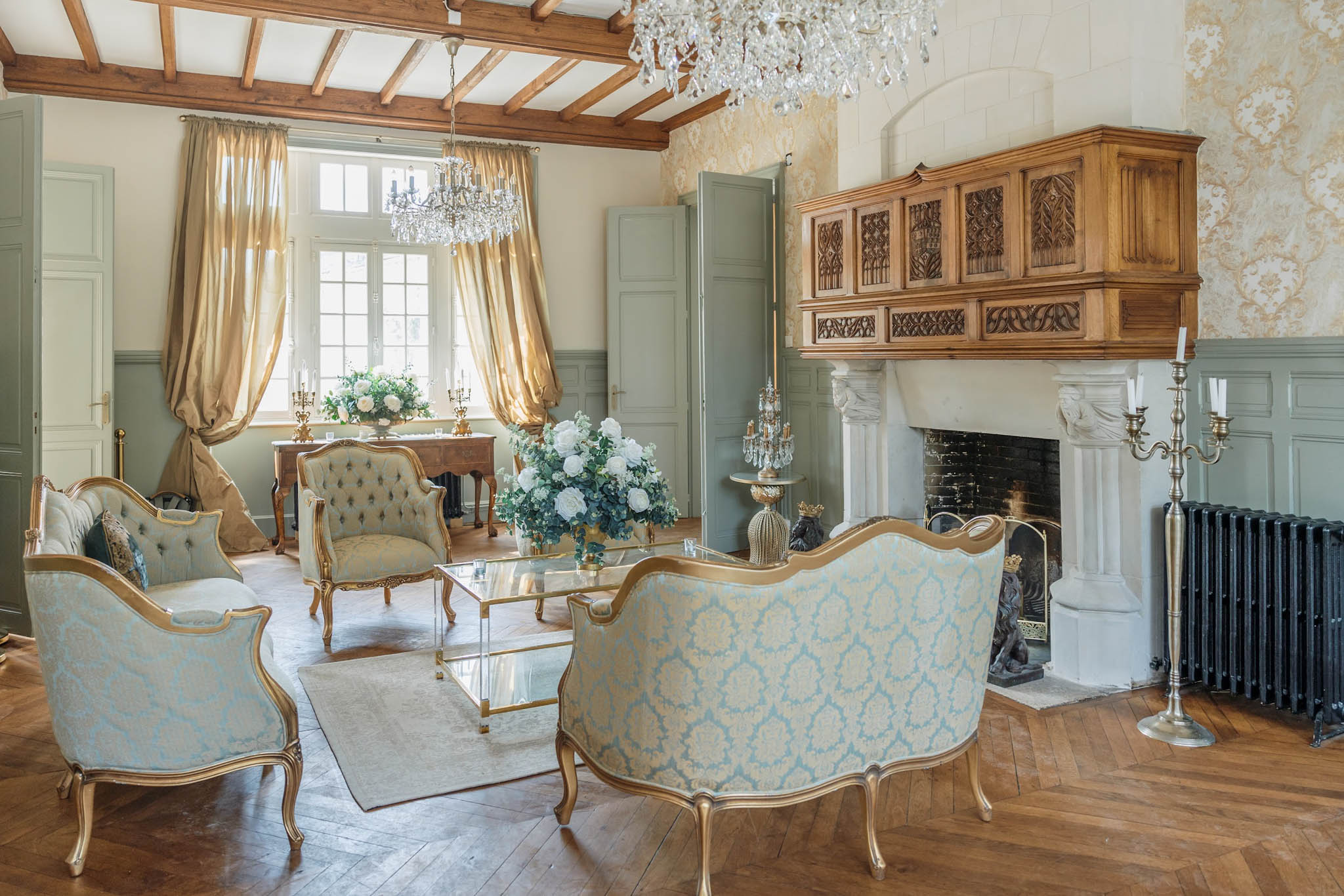 Chateau salon with sage panelling gold damask armchairs white marble fireplace and crystal chandeliers