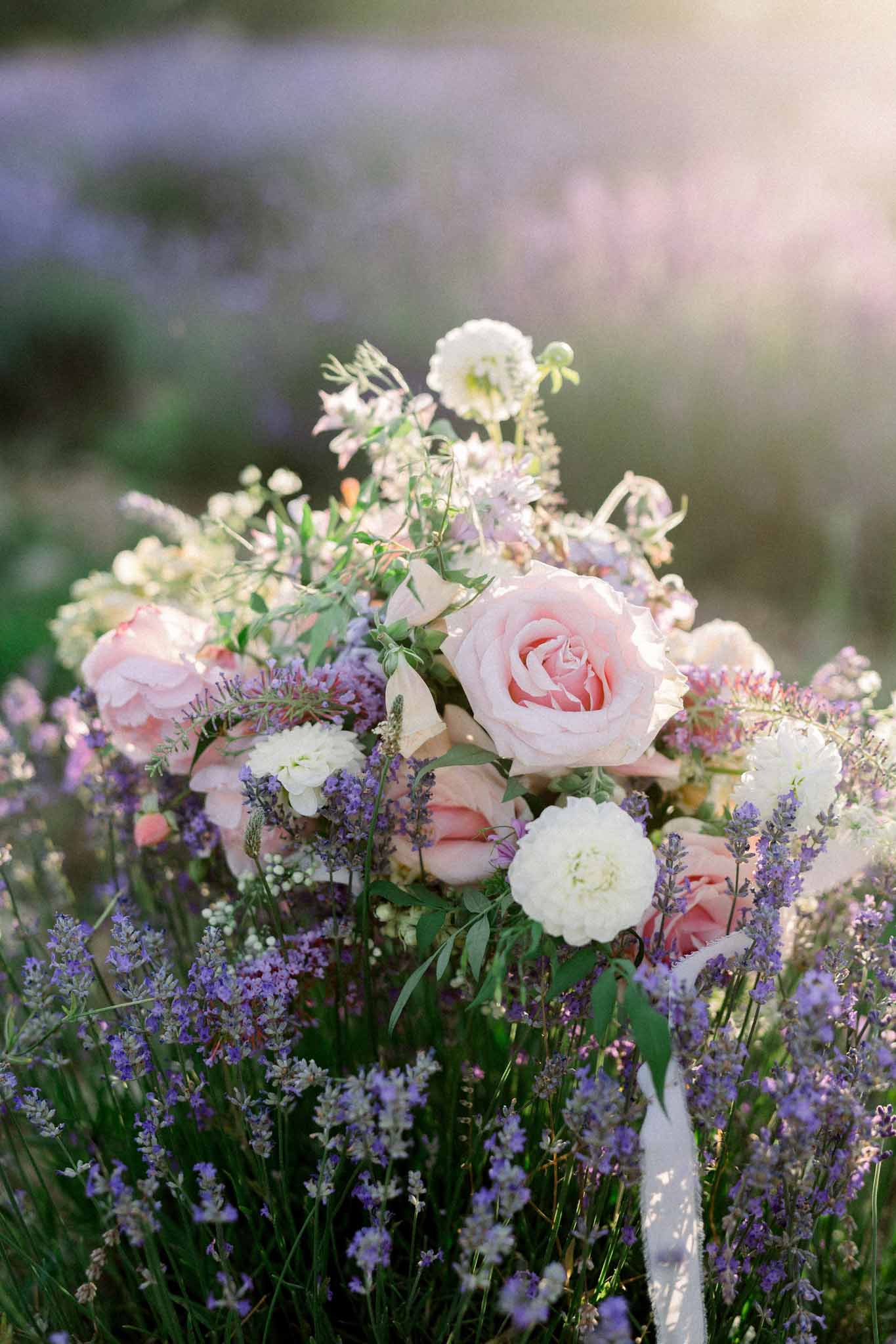 Close-up of bridal bouquet with pink roses, white dahlias, and lavender in field