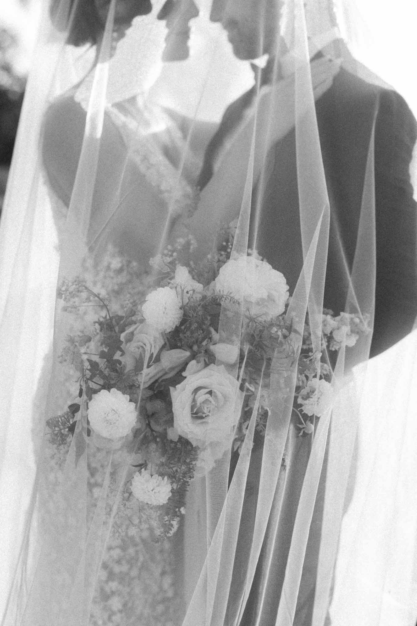 Bride and groom inside long veil in lavender fields, black and white photograph