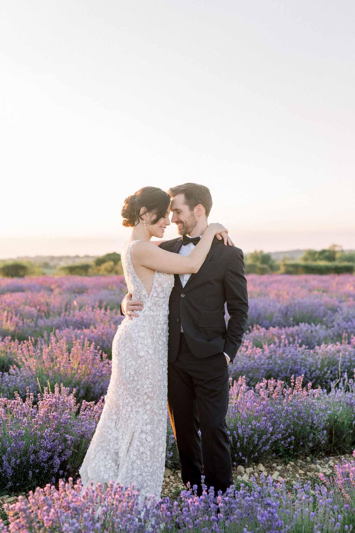 Close-up portrait of bride and groom faces in lavender fields with groom's hands on bride's hips