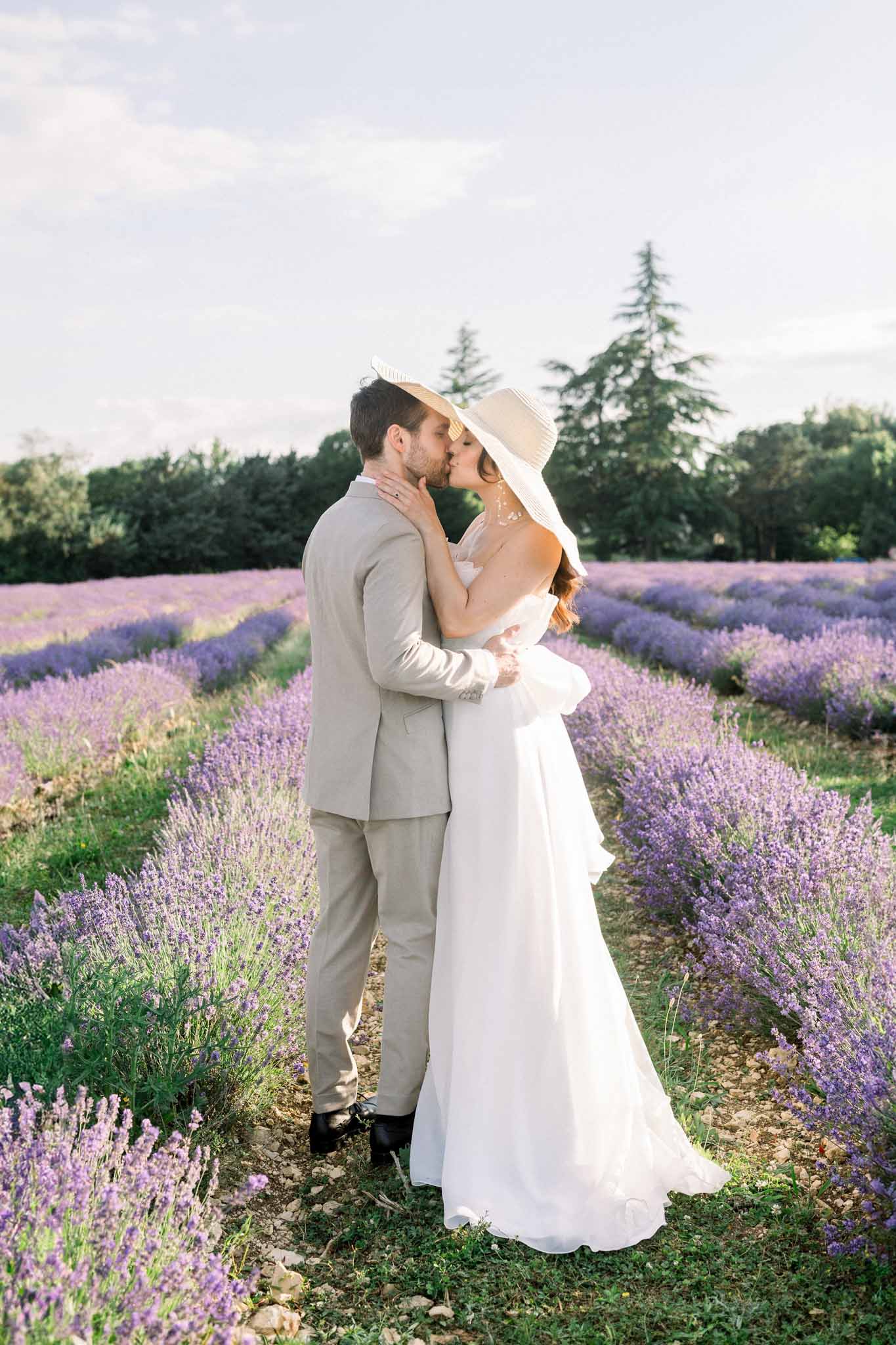 Bride and groom kissing in lavender fields, bride wearing a wide-brimmed hat