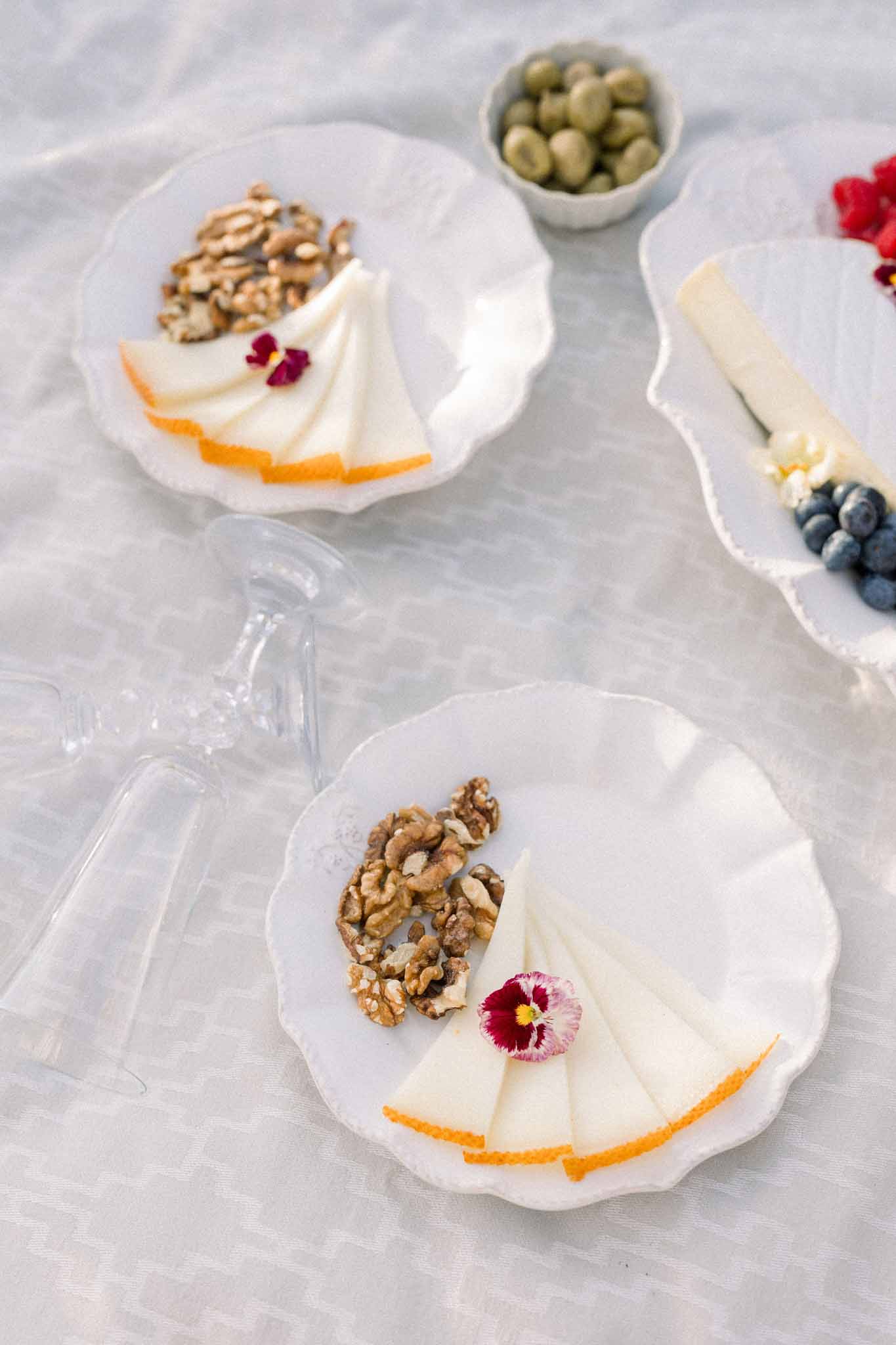 Flat lay of appetizer plates with sliced cheese, citrus, walnuts, and edible flowers on marble surface