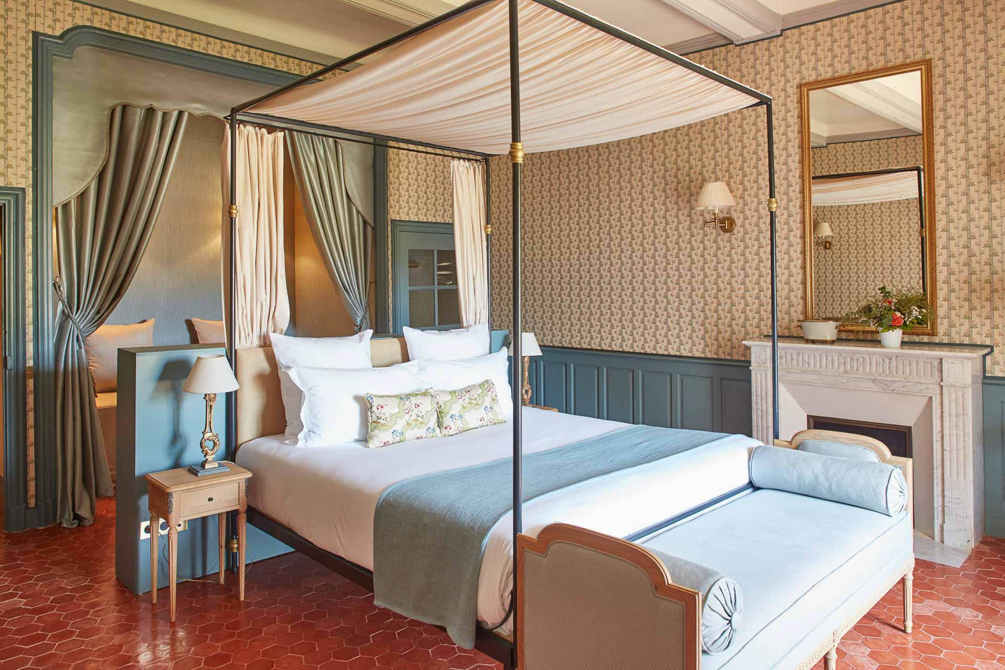 Chateau guest suite with black four-poster canopy bed, blue wood paneling, white marble fireplace, and terracotta tile floor