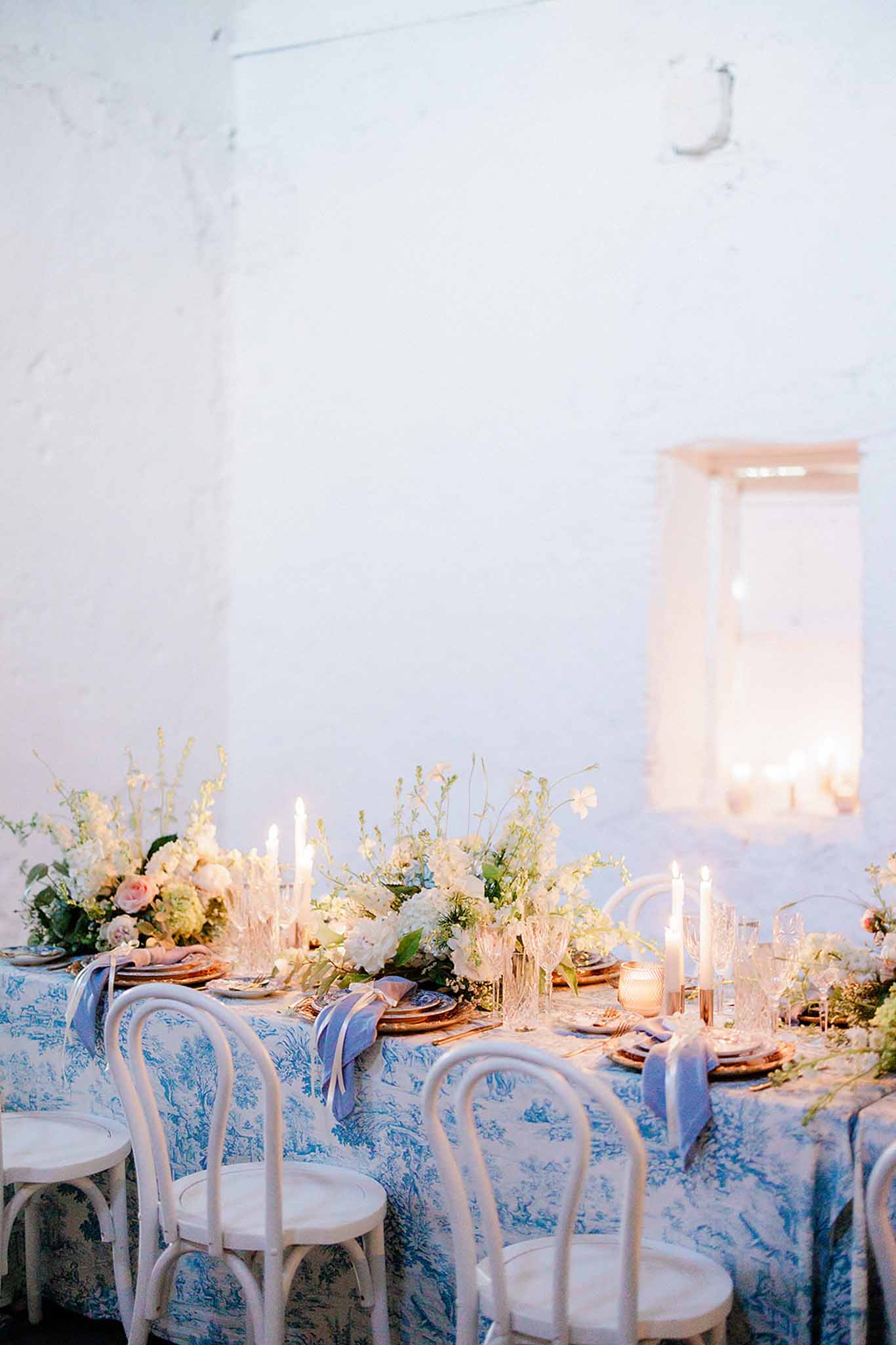 Long reception table with blue toile linens, copper chargers, and peach rose centerpieces