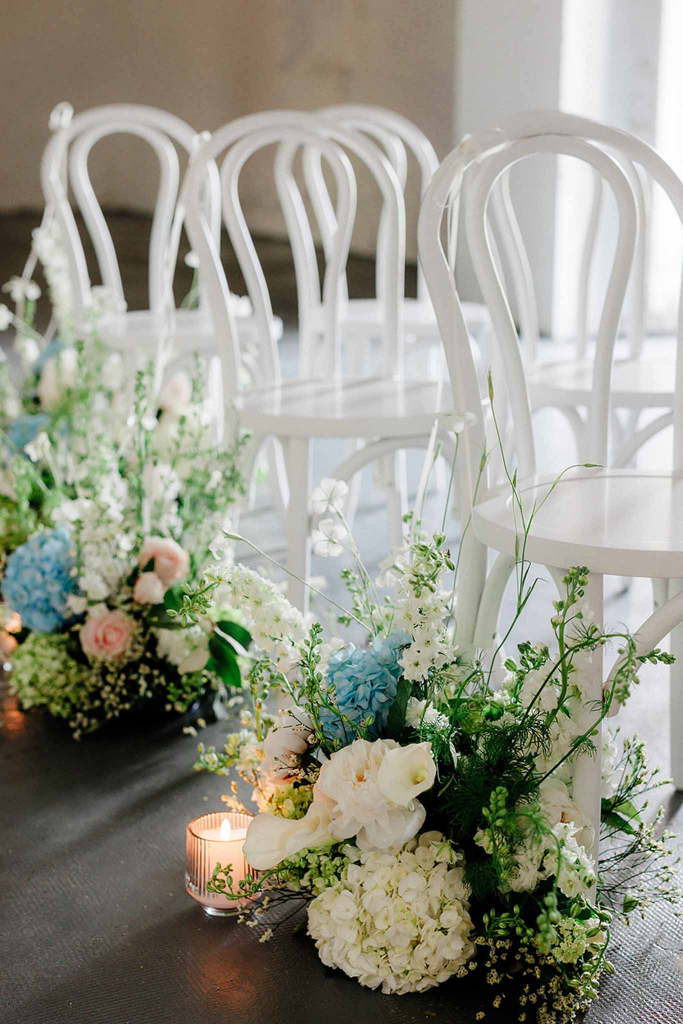 Ceremony aisle décor with white bentwood chairs, ivory hydrangeas, dusty blue hydrangeas and blush votives