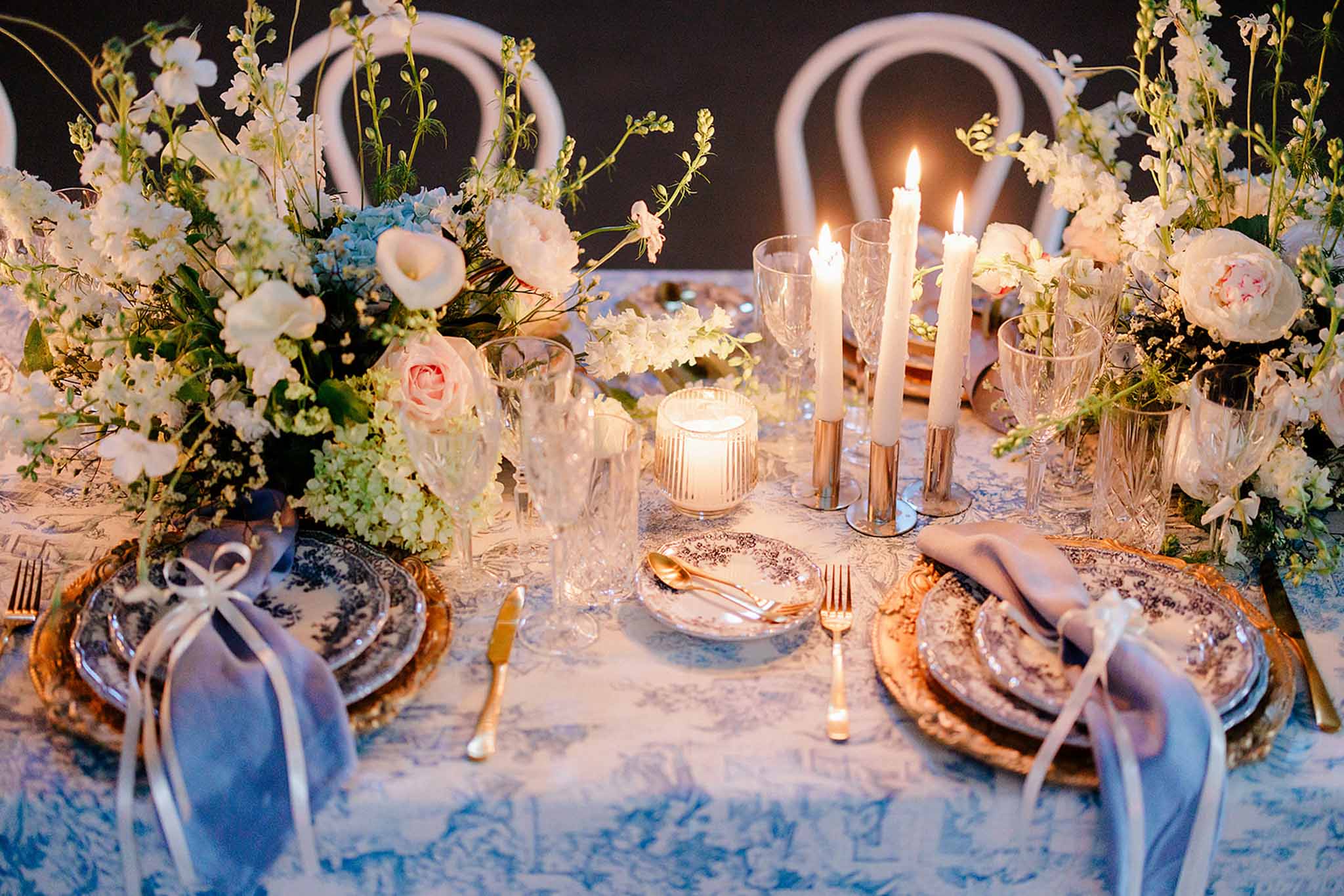 Evening table with blue and white damask linen, gold chargers, blue porcelain and white and blue hydrangea florals