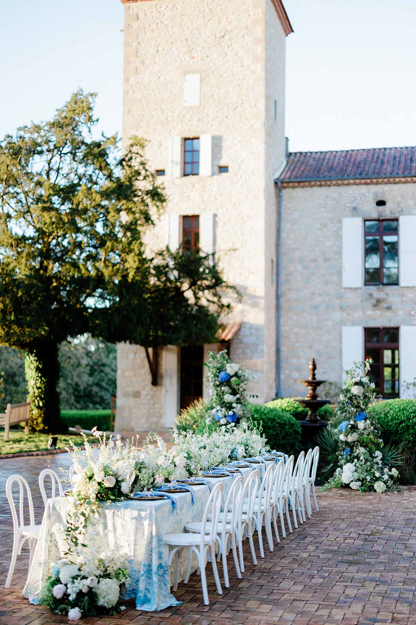 Long reception table set outside manor at Château de Trieux with guests and bride and groom