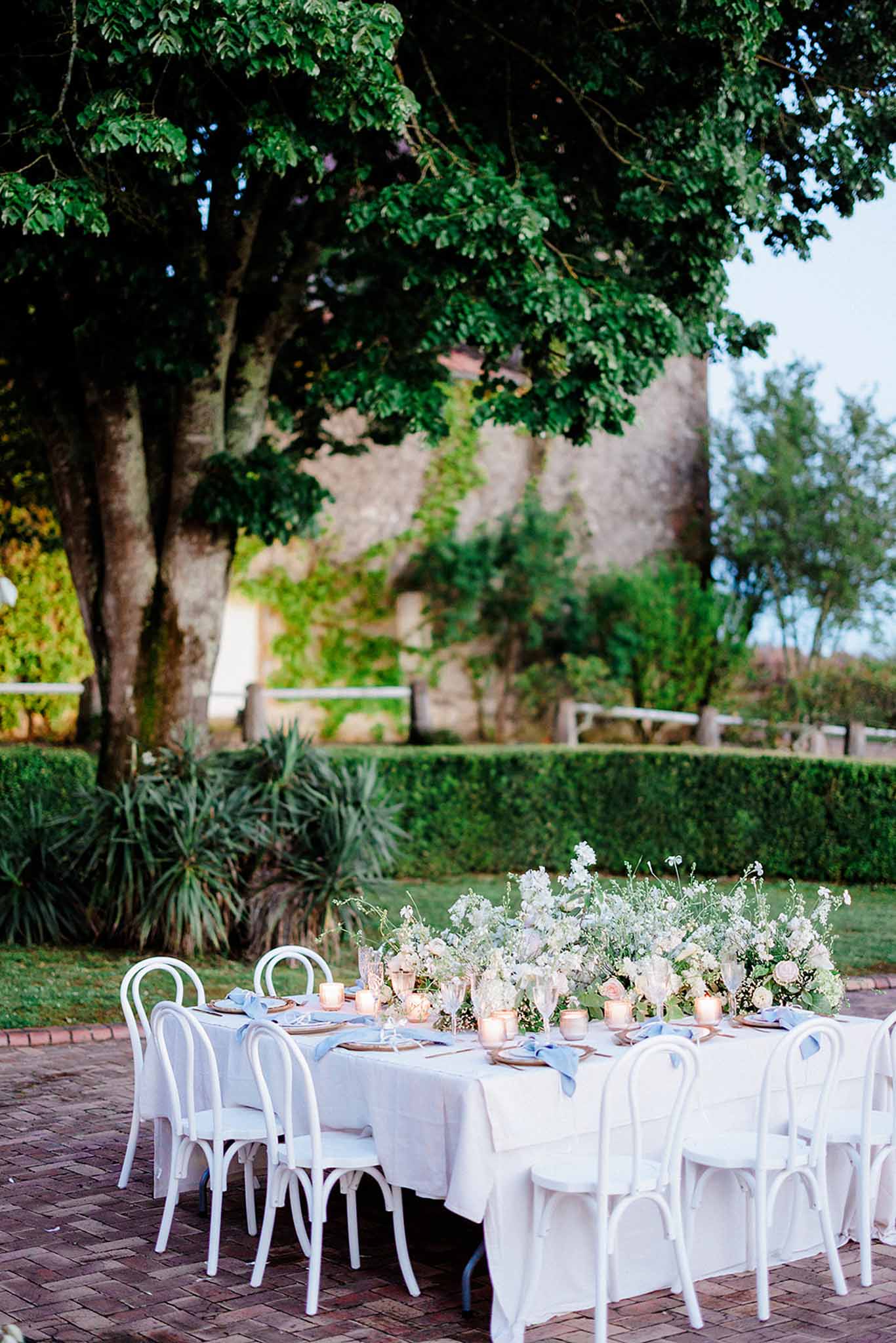 Square reception table with white chairs set in garden at Chateau Trieux photographed by M Mann