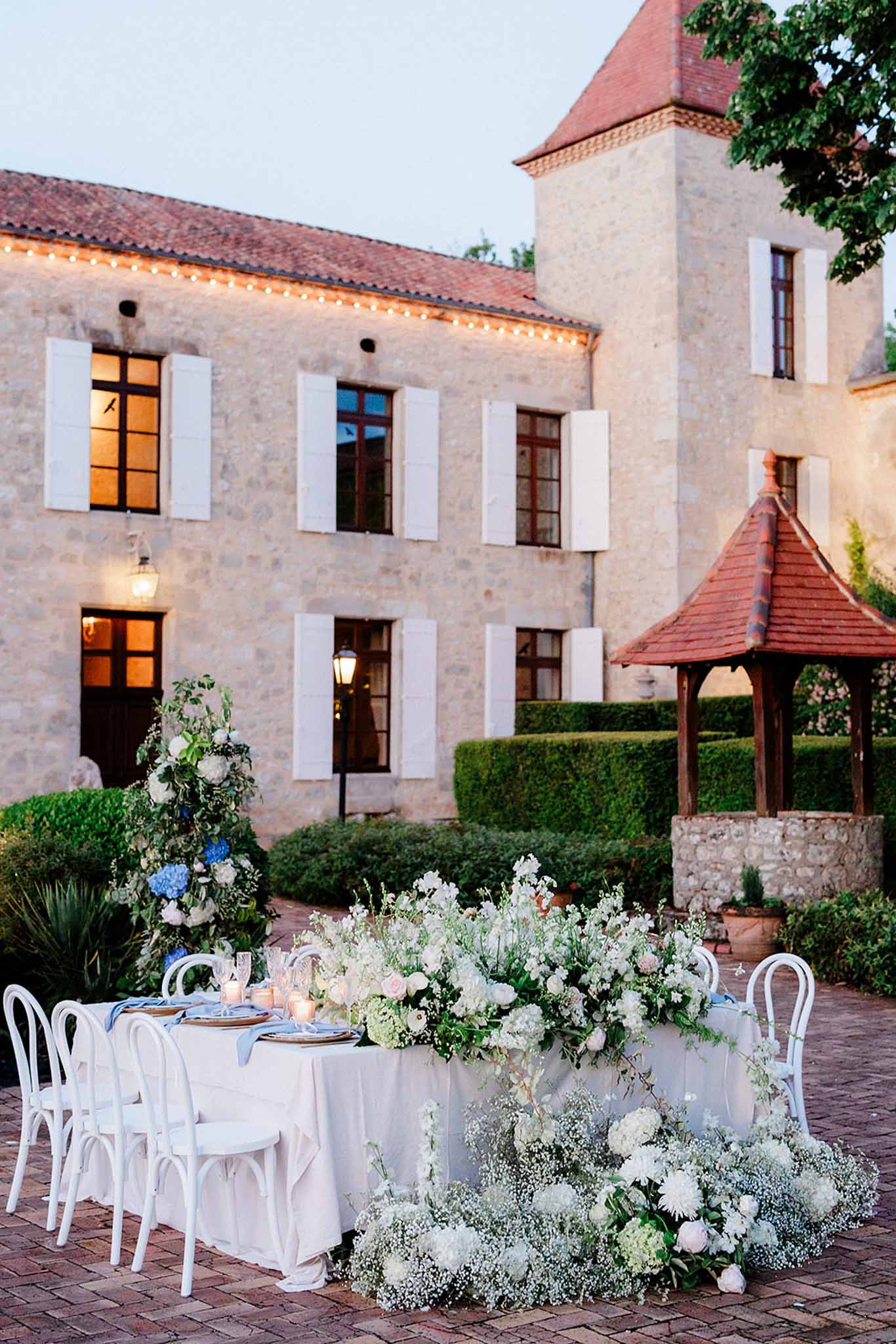 Twilight courtyard reception with floral installations and uplighting at historic stone villa