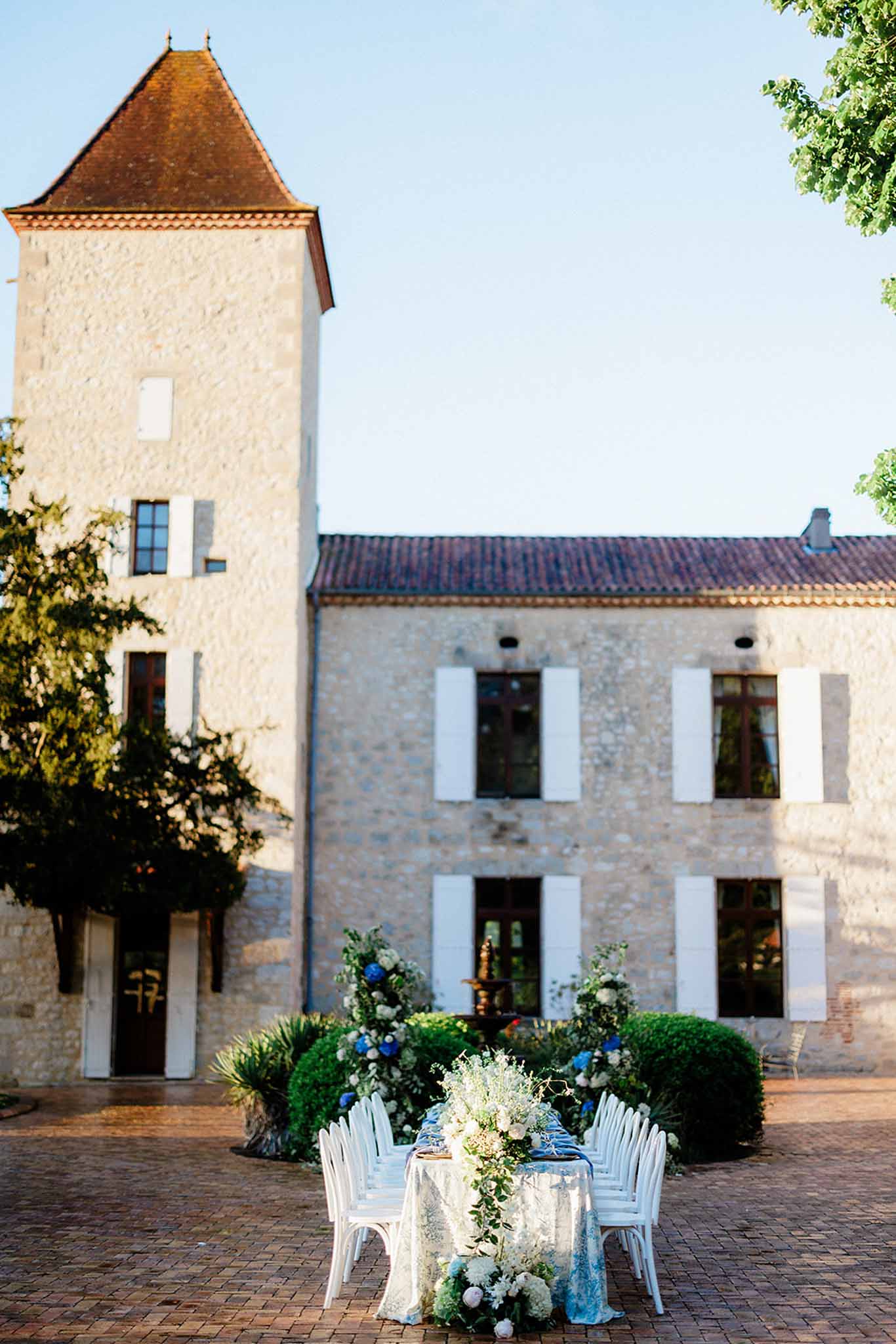 Sweetheart table in courtyard of stone estate with château tower, white roses and blue hydrangeas in pots