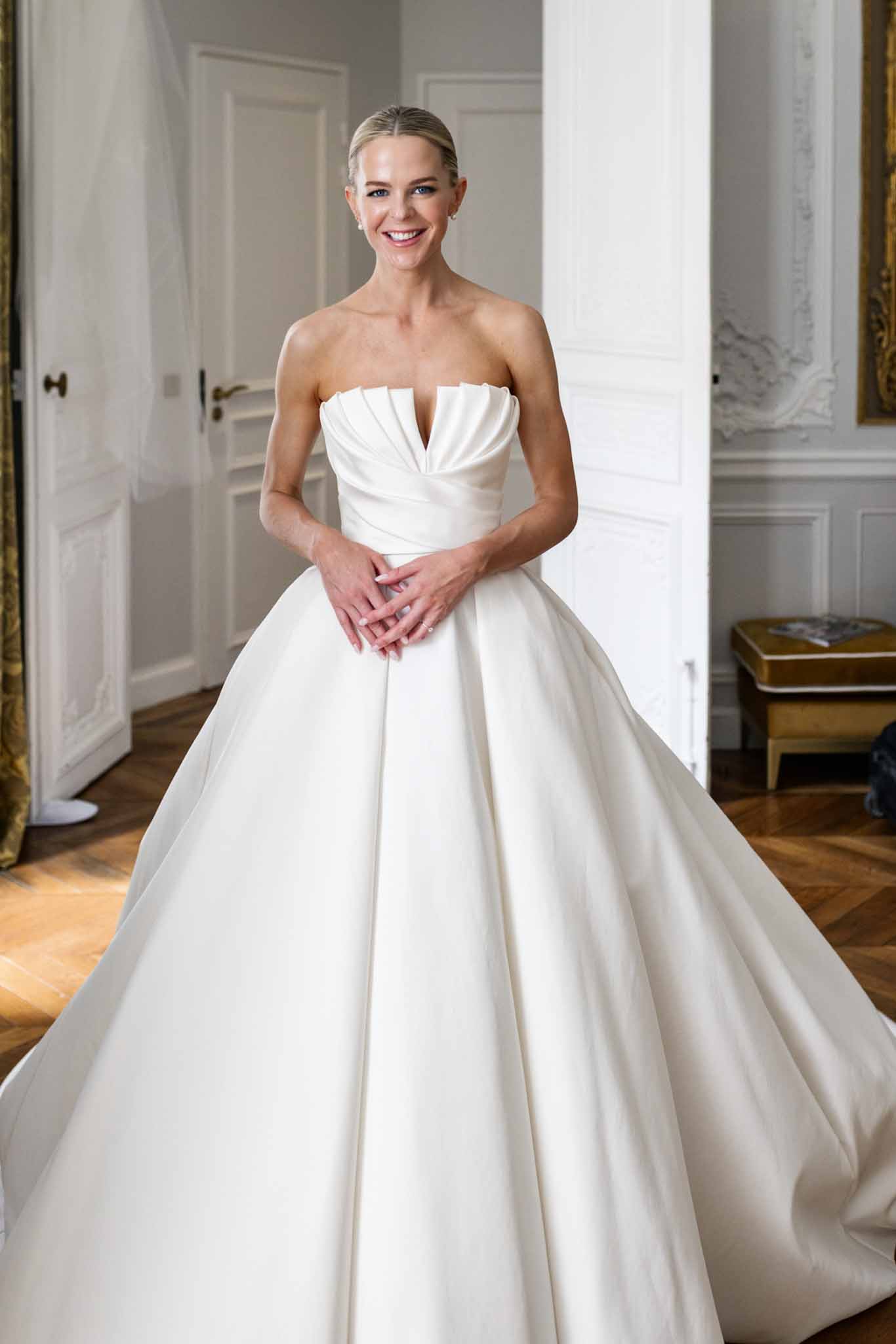 Bride in strapless ivory ball gown poses in neoclassical hallway with herringbone floors and paneled doors