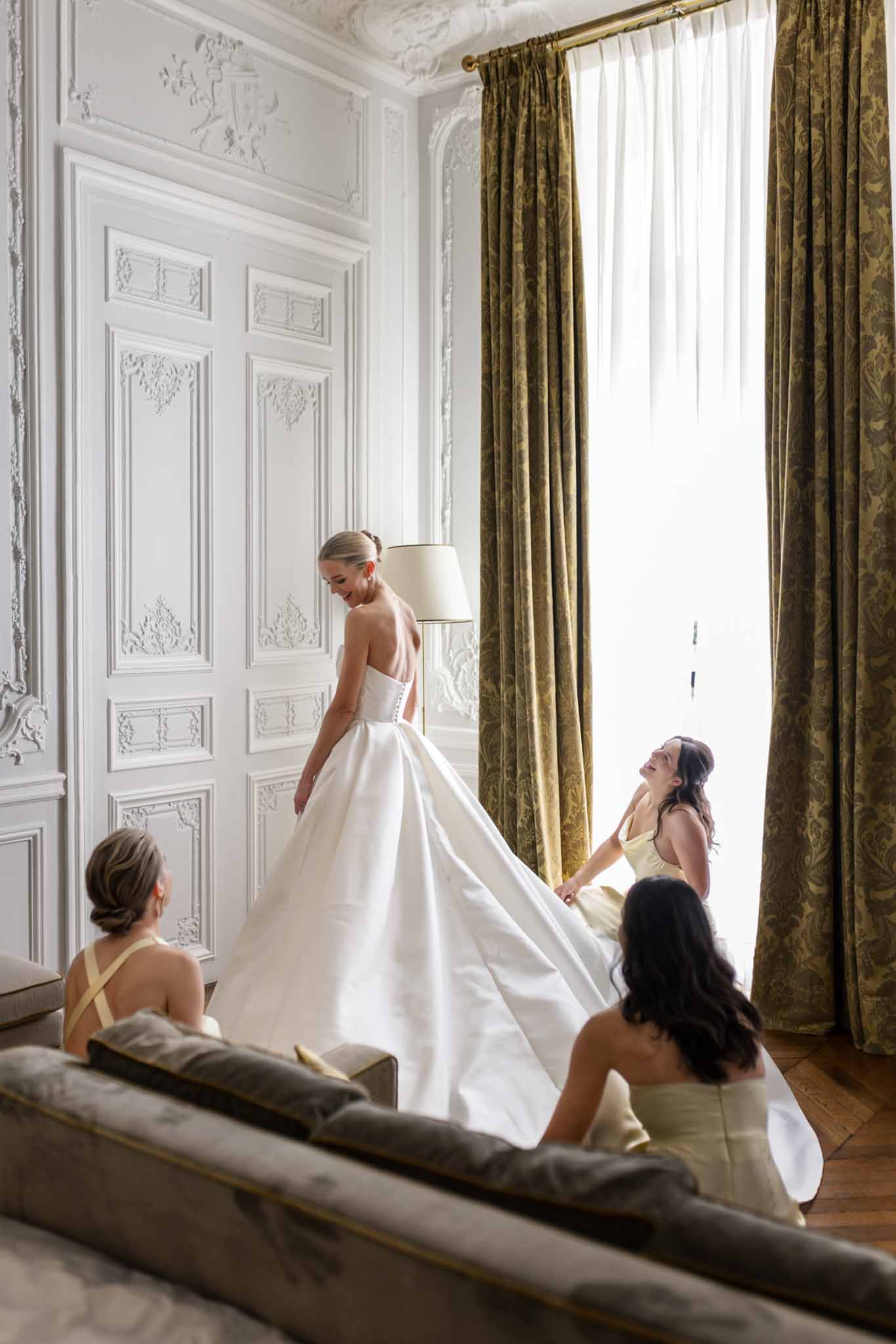 Bridesmaid helping bride fix the back of her wedding gown while getting ready at Château de Villette