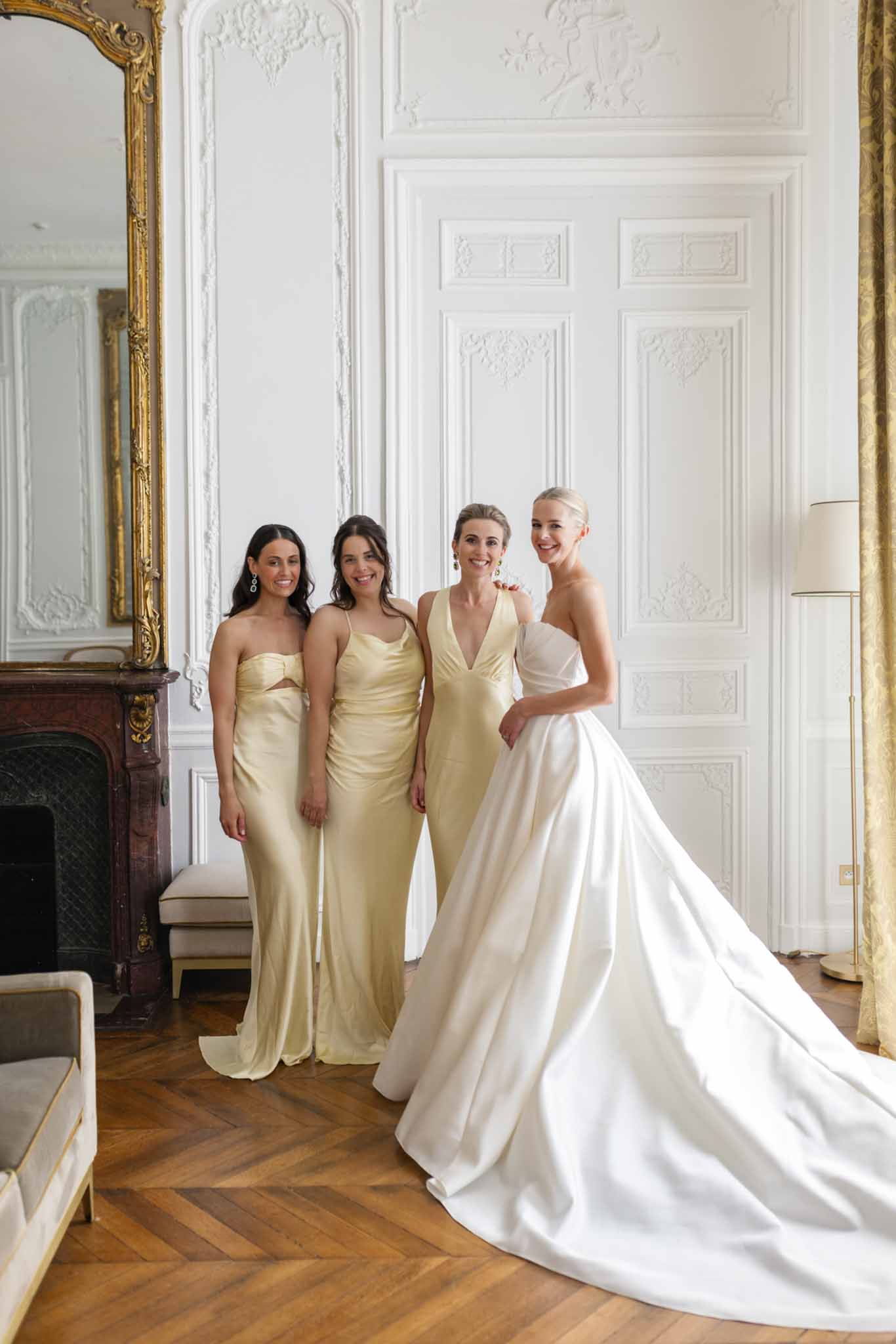 Bride in ivory gown with three bridesmaids in champagne-gold dresses posing in an ornate classical interior