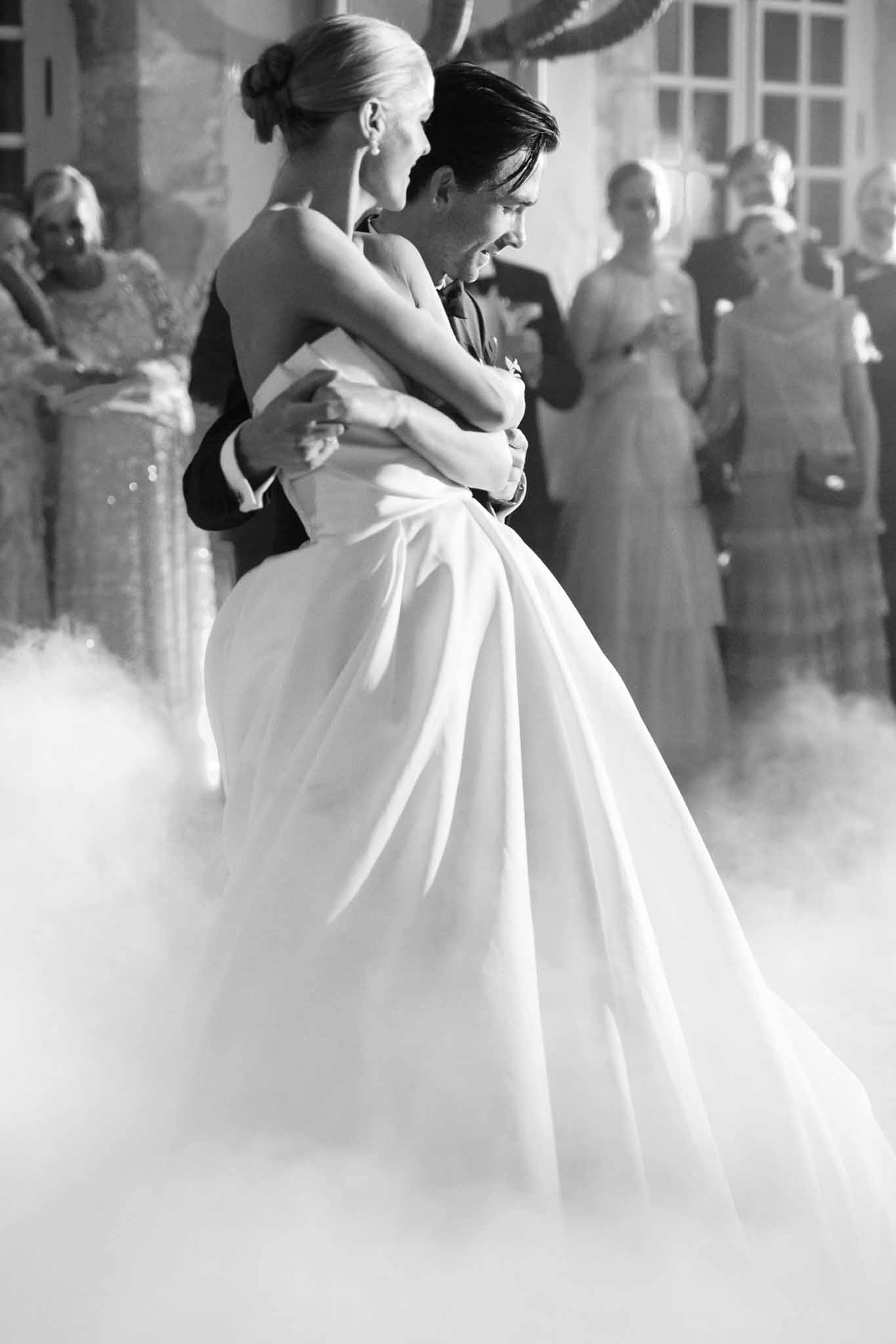 Black and white photo of groom lifting bride during first dance surrounded by dry ice fog