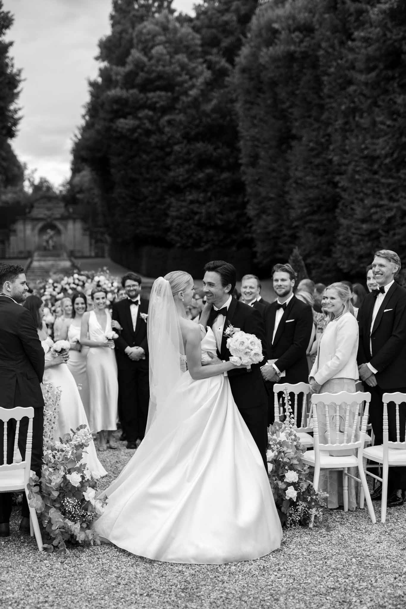Black and white garden ceremony, bride and groom at altar, 50-75 guests in Chiavari chairs, stone chapel in background