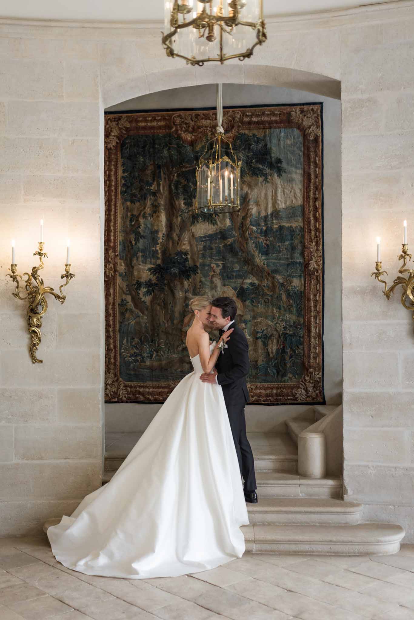 Bride and groom kissing in neoclassical interior with gilded landscape painting, brass sconces, and stone floors
