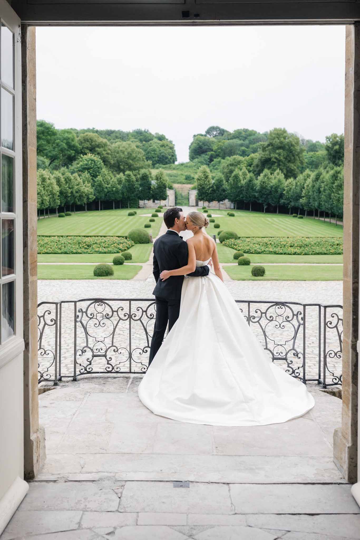 Bride and groom kissing on stone terrace overlooking formal French garden at Chateau de Villette