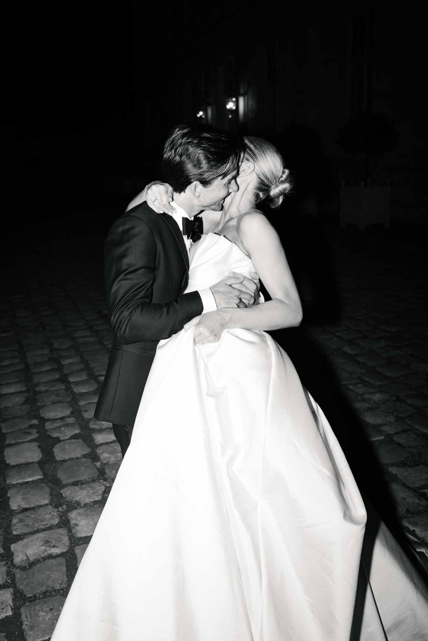Black and white photo of bride and groom sharing their first dance on an outdoor stone courtyard at night