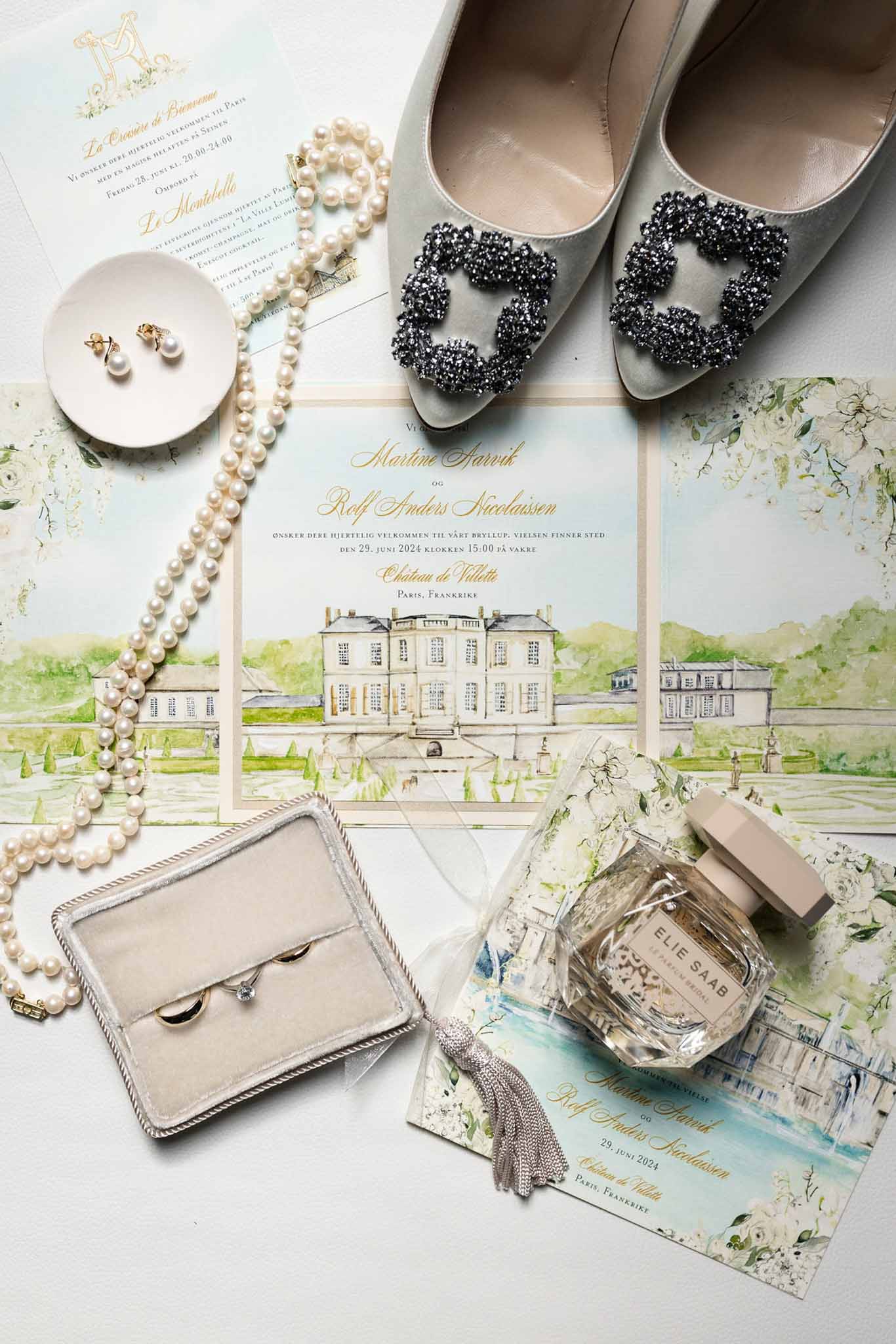 Flat lay of bridal accessories including pearl necklace, ivory silk pumps with crystal buckles, wedding bands and stationery