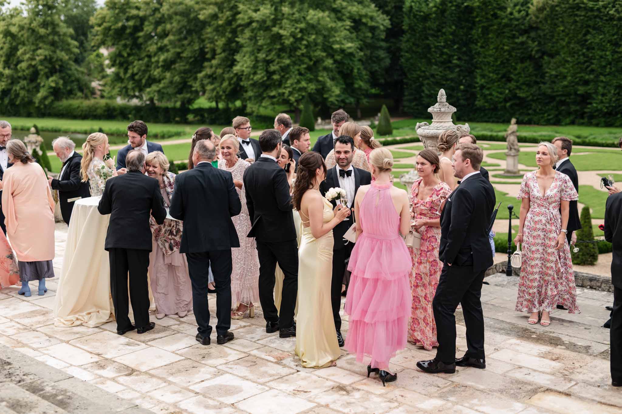 Guests mingling on stone terrace during cocktail hour at classical French estate with formal gardens and topiary