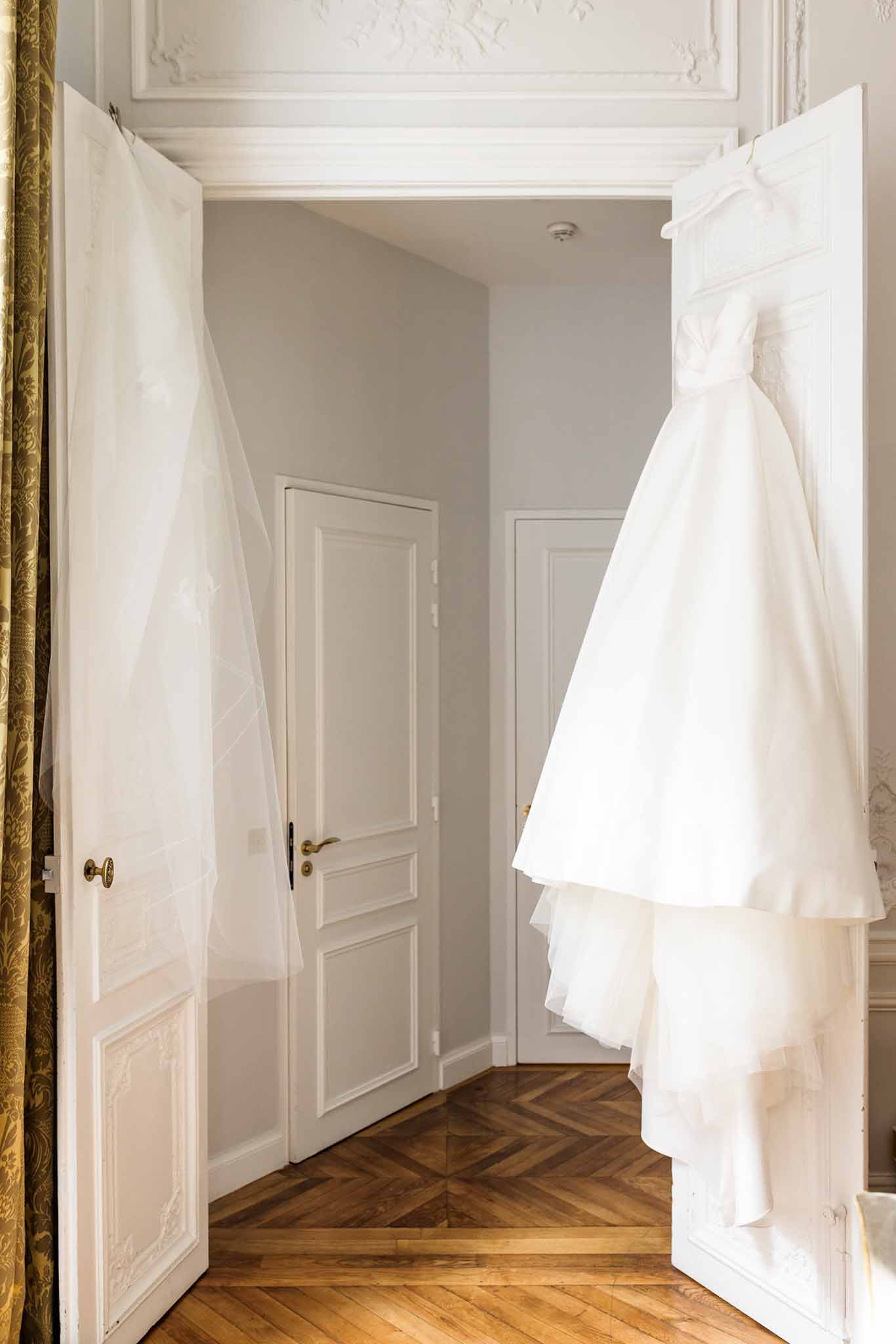 Ivory and cream tulle wedding gown hanging on white paneled doors in formal bridal suite with herringbone parquet floor