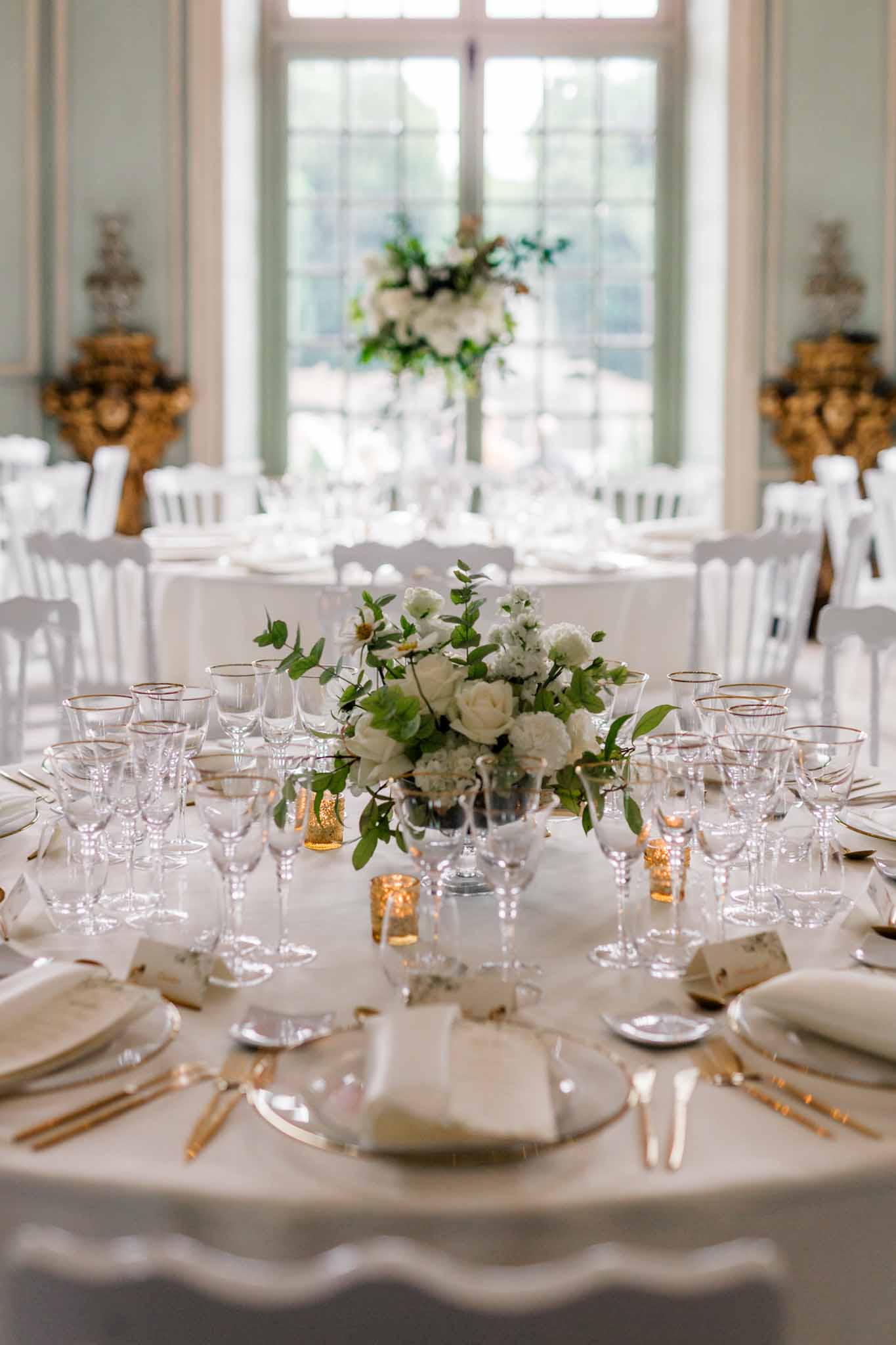 Reception table with ivory linens, gold flatware, ivory rose centerpieces, and gold votives