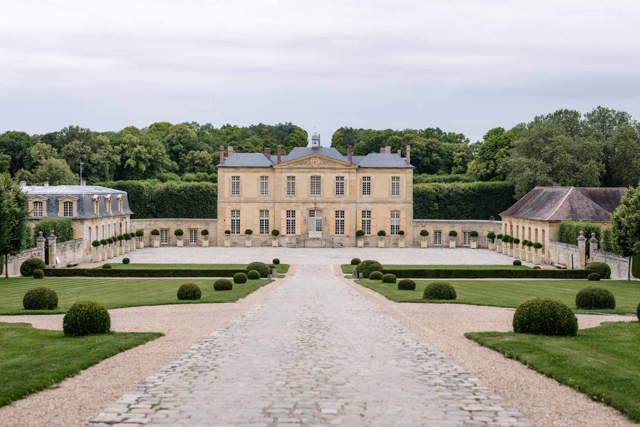 Wide view of classical French chateau with mansard roof, topiary gardens, and gravel forecourt