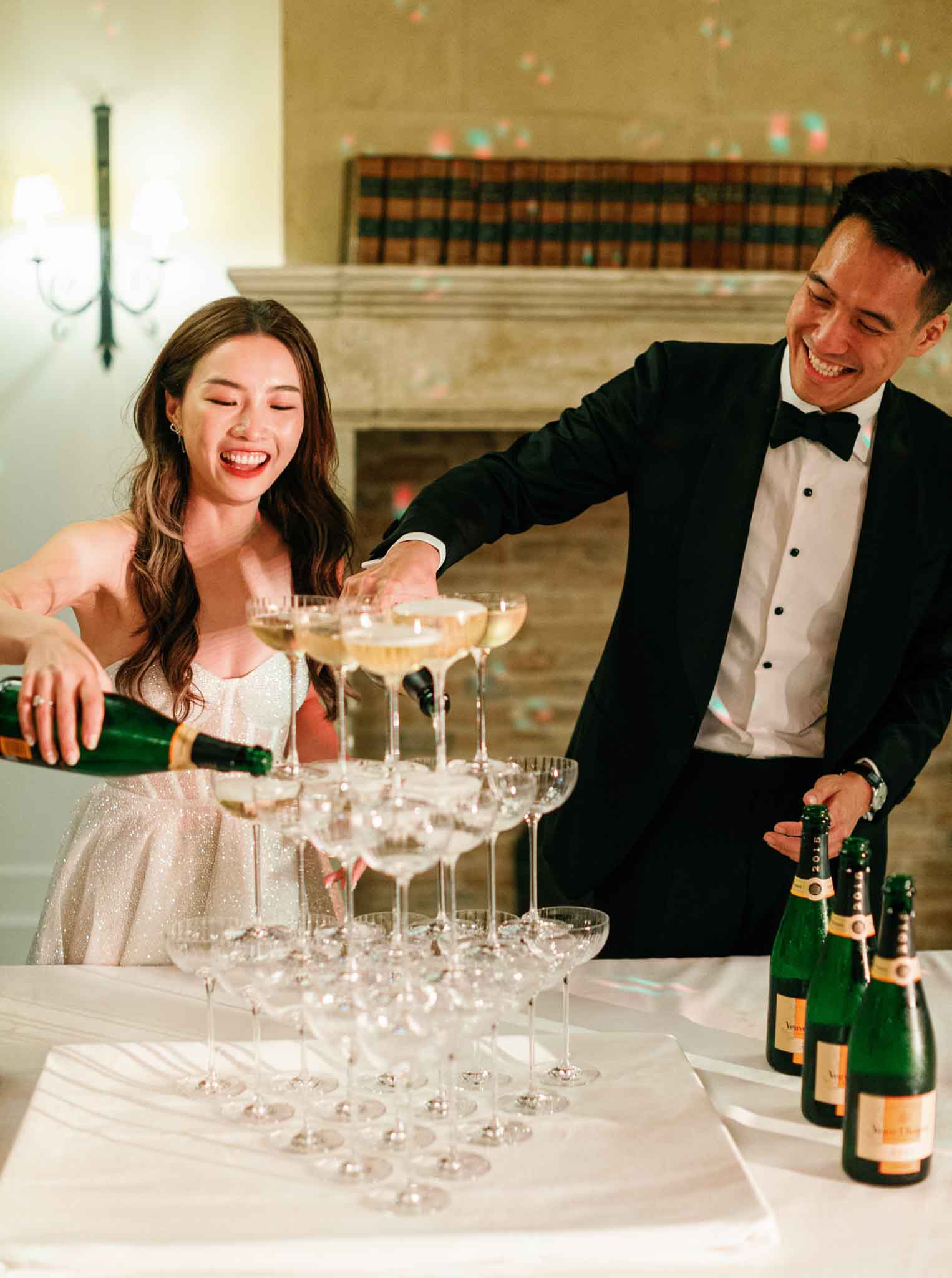 Bride and groom pouring champagne into coupe glass pyramid at indoor reception