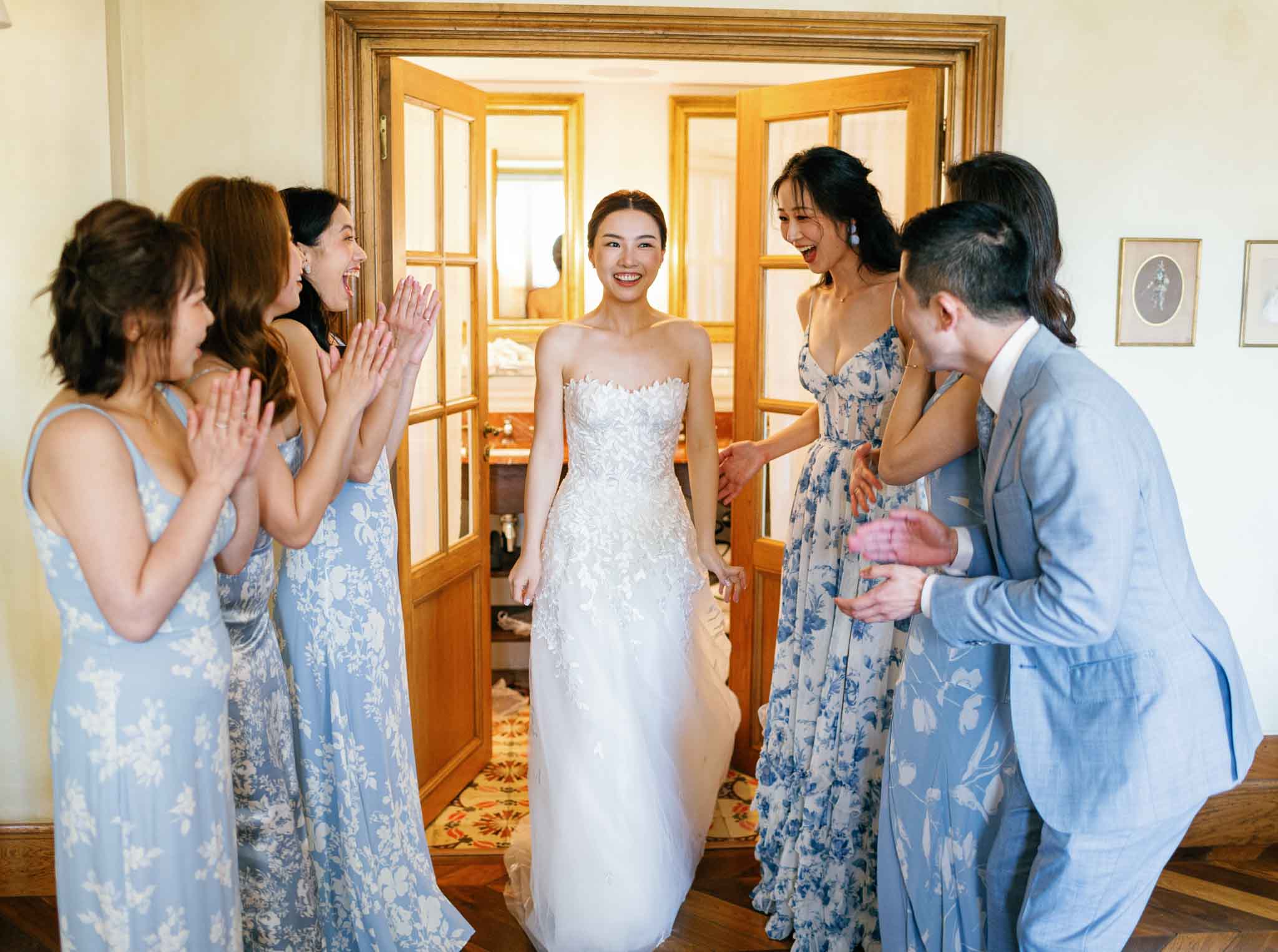 Bride surrounded by bridal party in blue floral dresses celebrating in classical room with gold doors