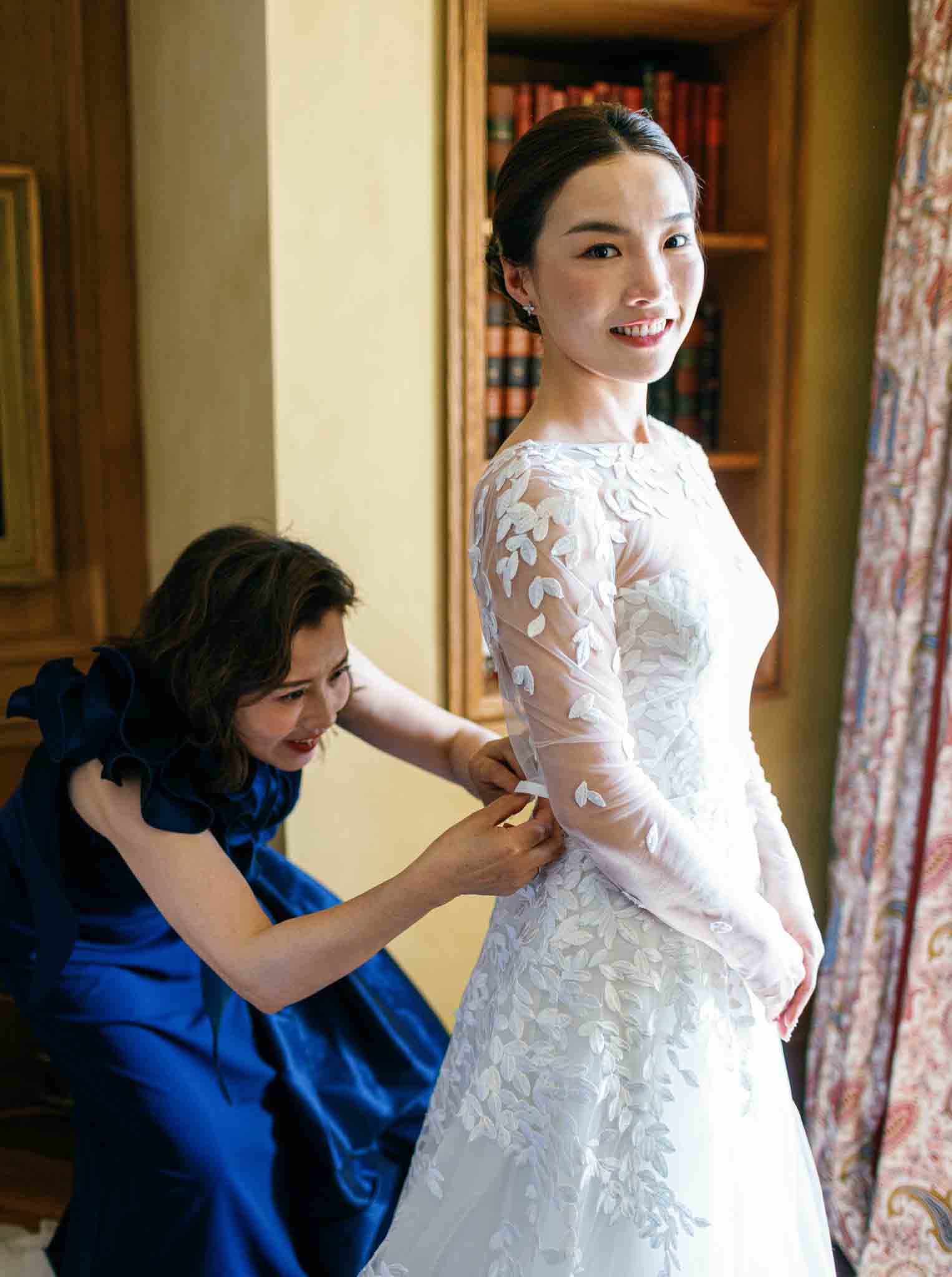 Bride in white lace gown with three-quarter sleeves being attended to in elegant hotel corridor