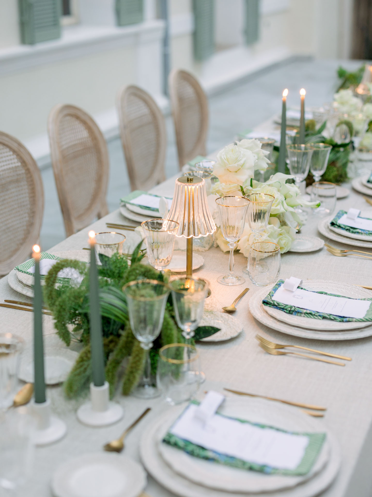 Formal reception table with gold flatware, green tapered candles, and white rose centerpieces