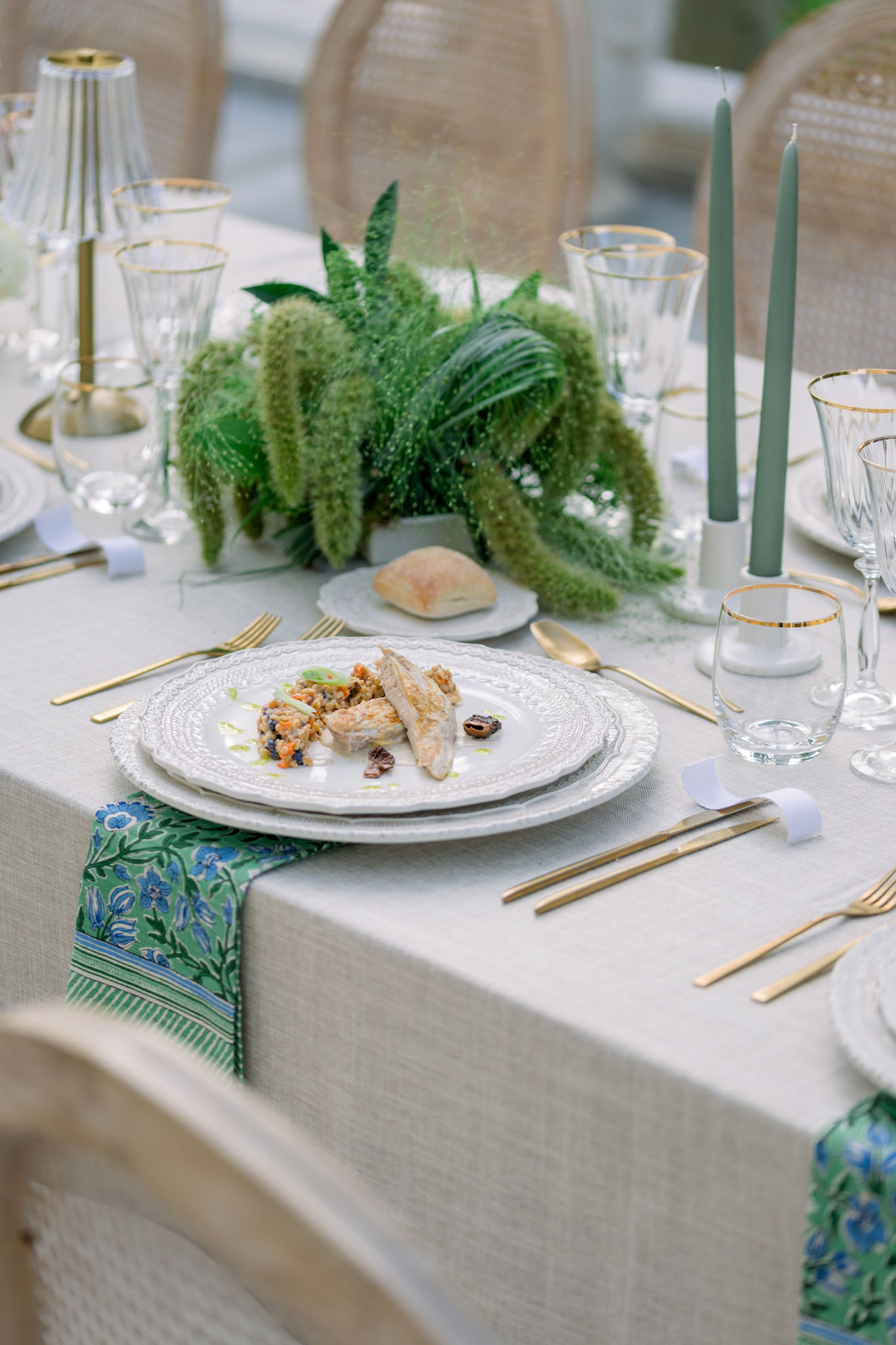 Reception place setting with plated fish course, botanical-print napkin, green fern centerpiece, and gold flatware