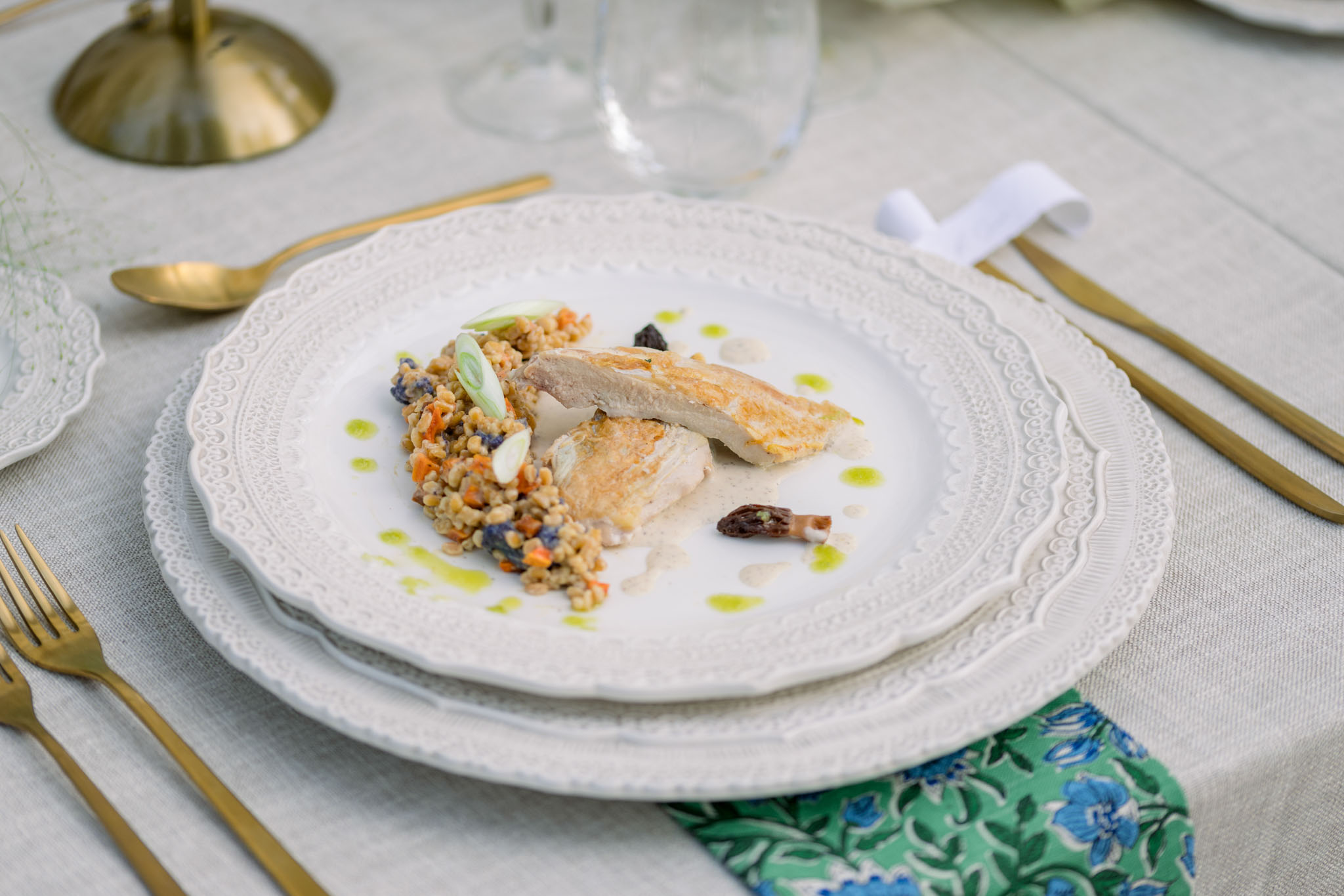 Plated fish course with lentils and vegetables on white charger plate with gold flatware at reception