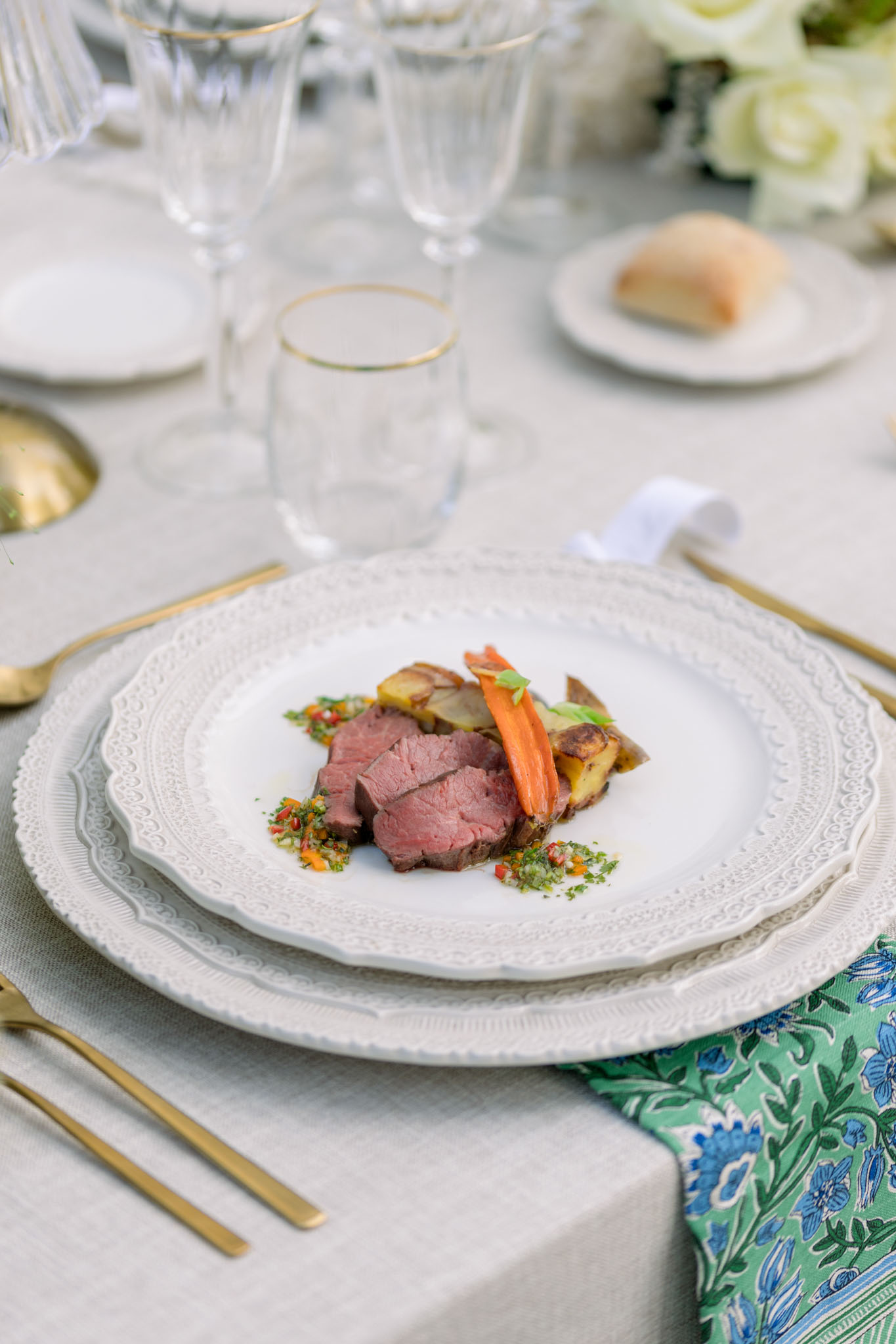 Plated beef fillet with roasted potatoes on white textured plate, gold flatware and green patterned napkin
