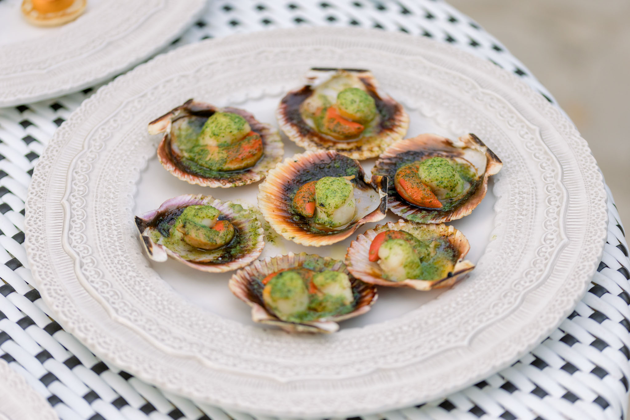 Eight scallops on half shell with herb oil served on white embossed plate with geometric linen