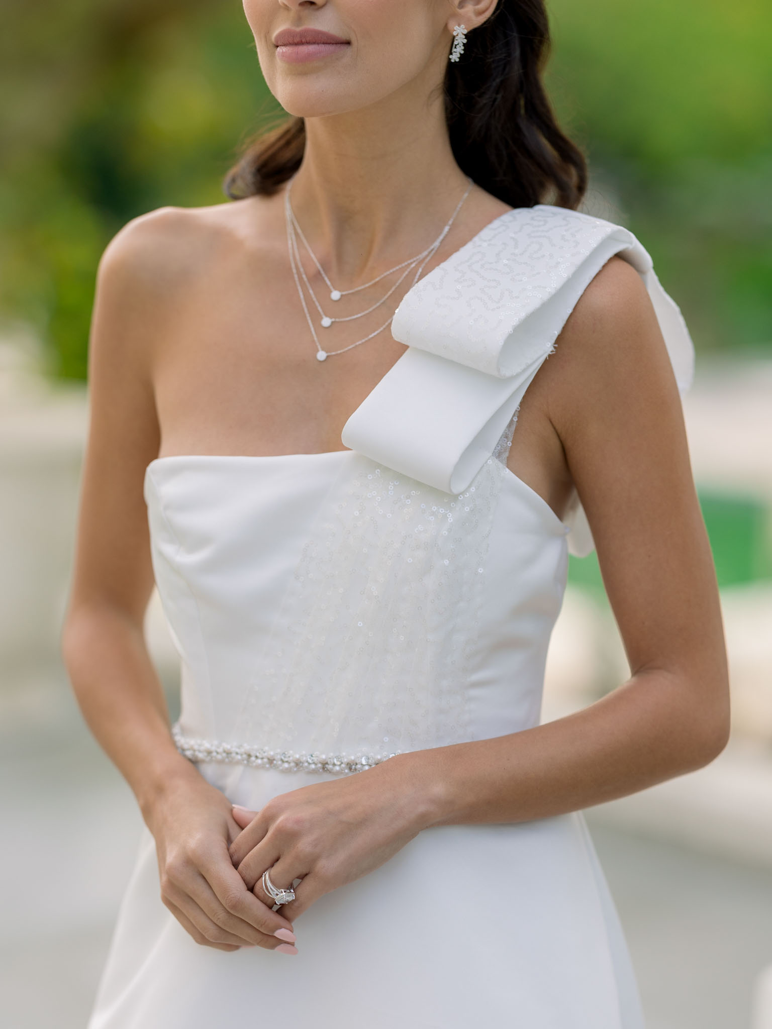 Close-up portrait of bride in ivory one-shoulder gown with bow detail, layered pearl necklaces and diamond ring