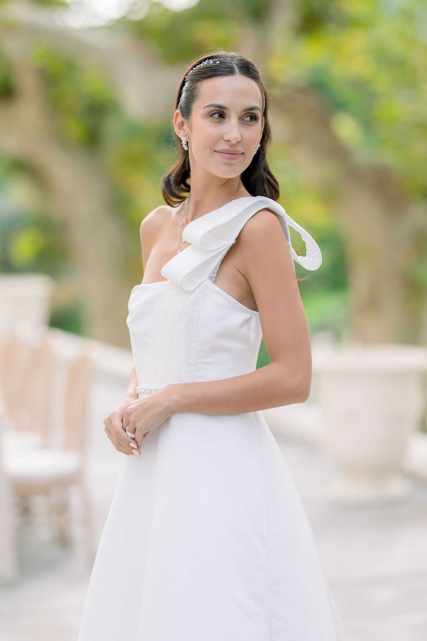 Bride in ivory one-shoulder ruffled gown with pearl accessories against ivy-covered wall