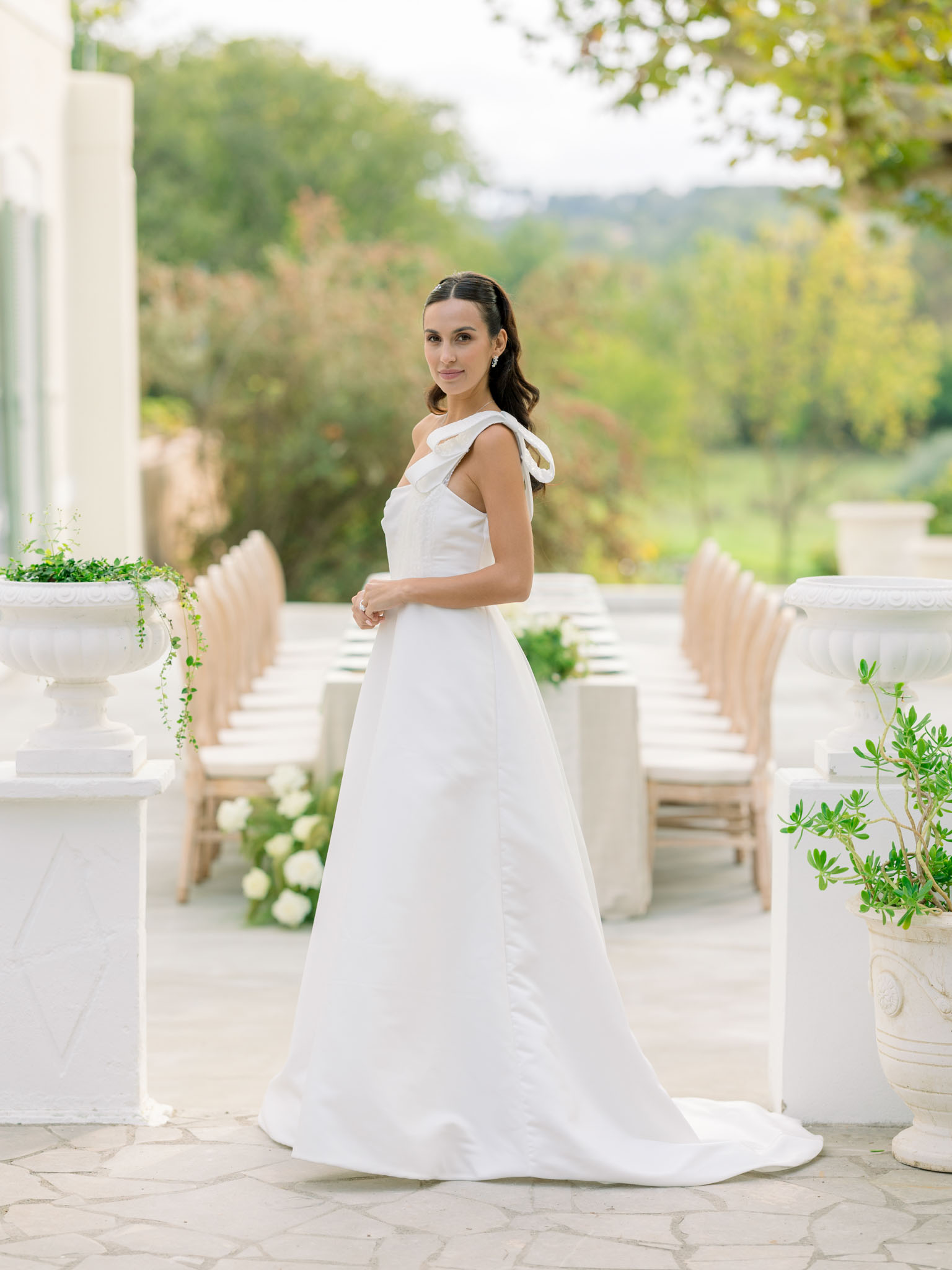 Bride in ivory sleeveless A-line gown on stone terrace with classical urns and countryside backdrop