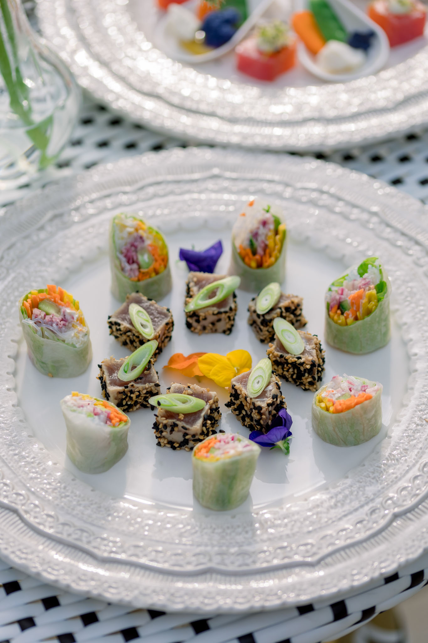 Plated canapes with cucumber rolls and sesame-crusted protein topped with purple and yellow edible flowers