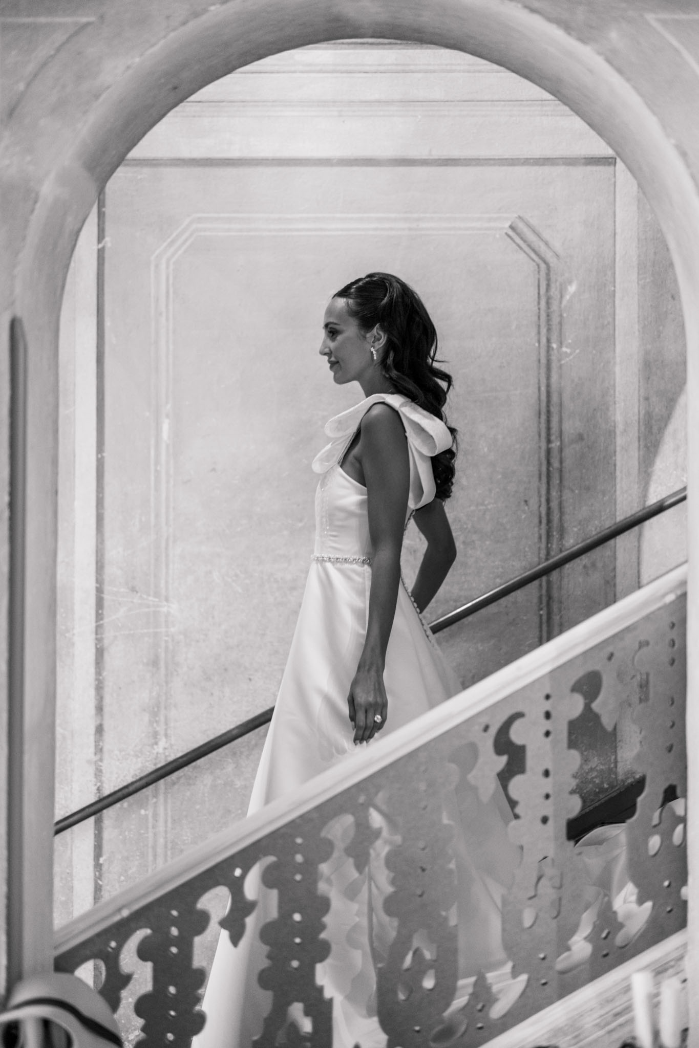 Black and white bridal portrait on a staircase with curved archway and ornate metal railing
