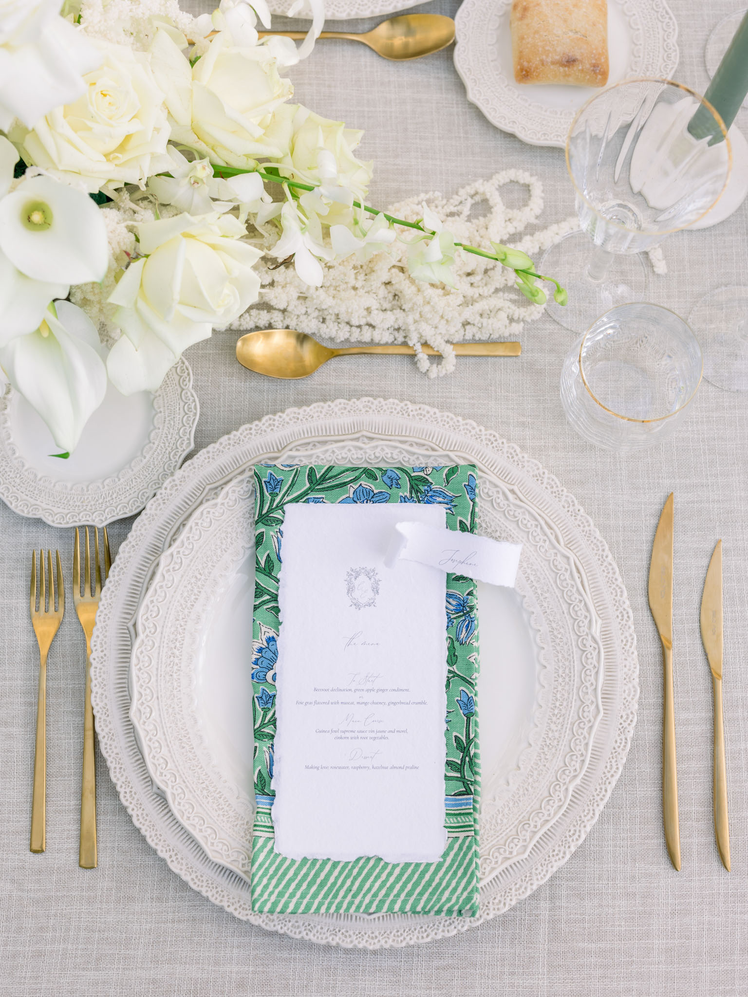 Individual place setting with botanical-bordered menu card, gold flatware, ivory roses, and pearl beaded garland