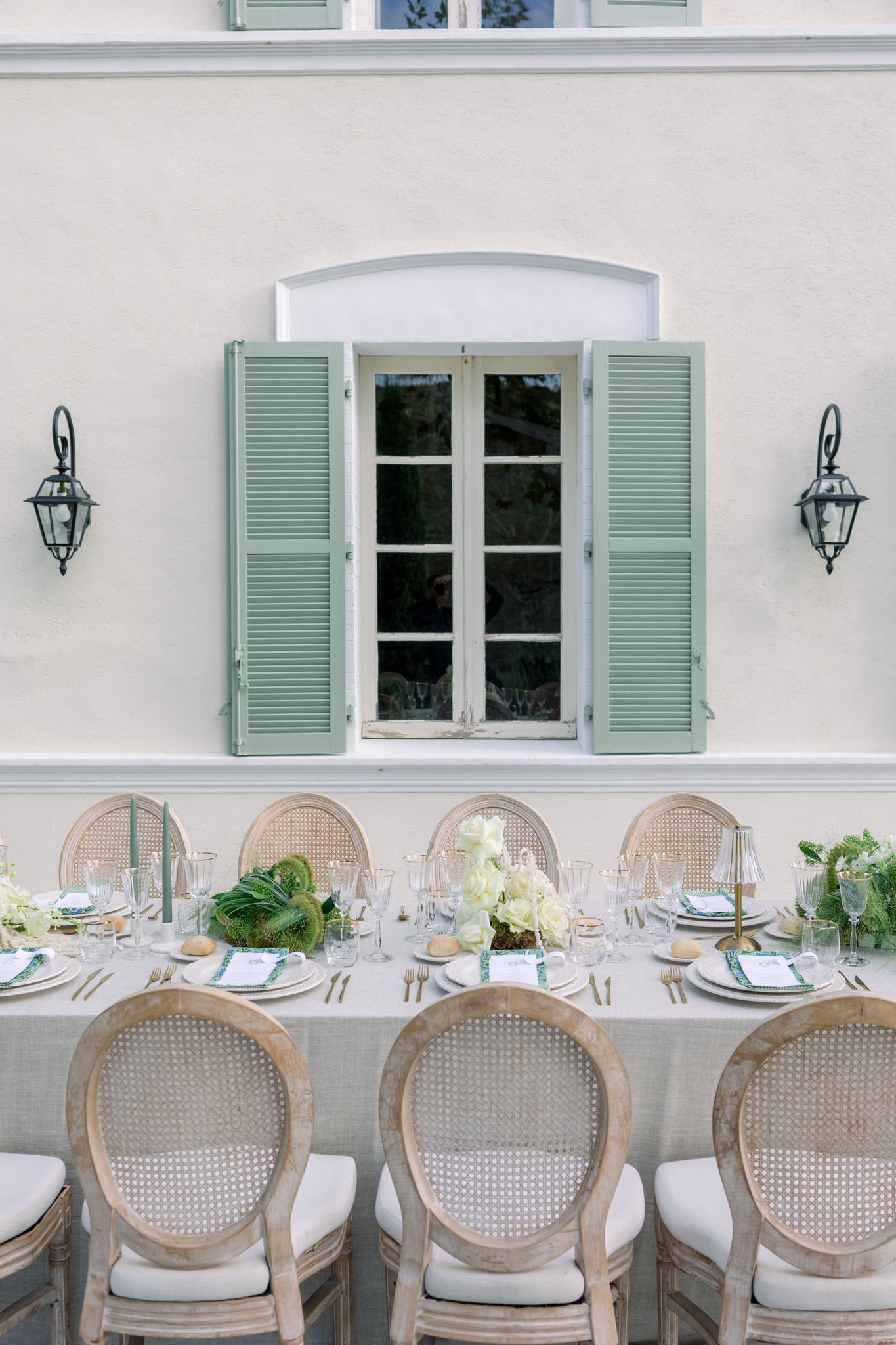 Reception table with white hydrangea centerpieces and rattan chairs against a facade with green shutters